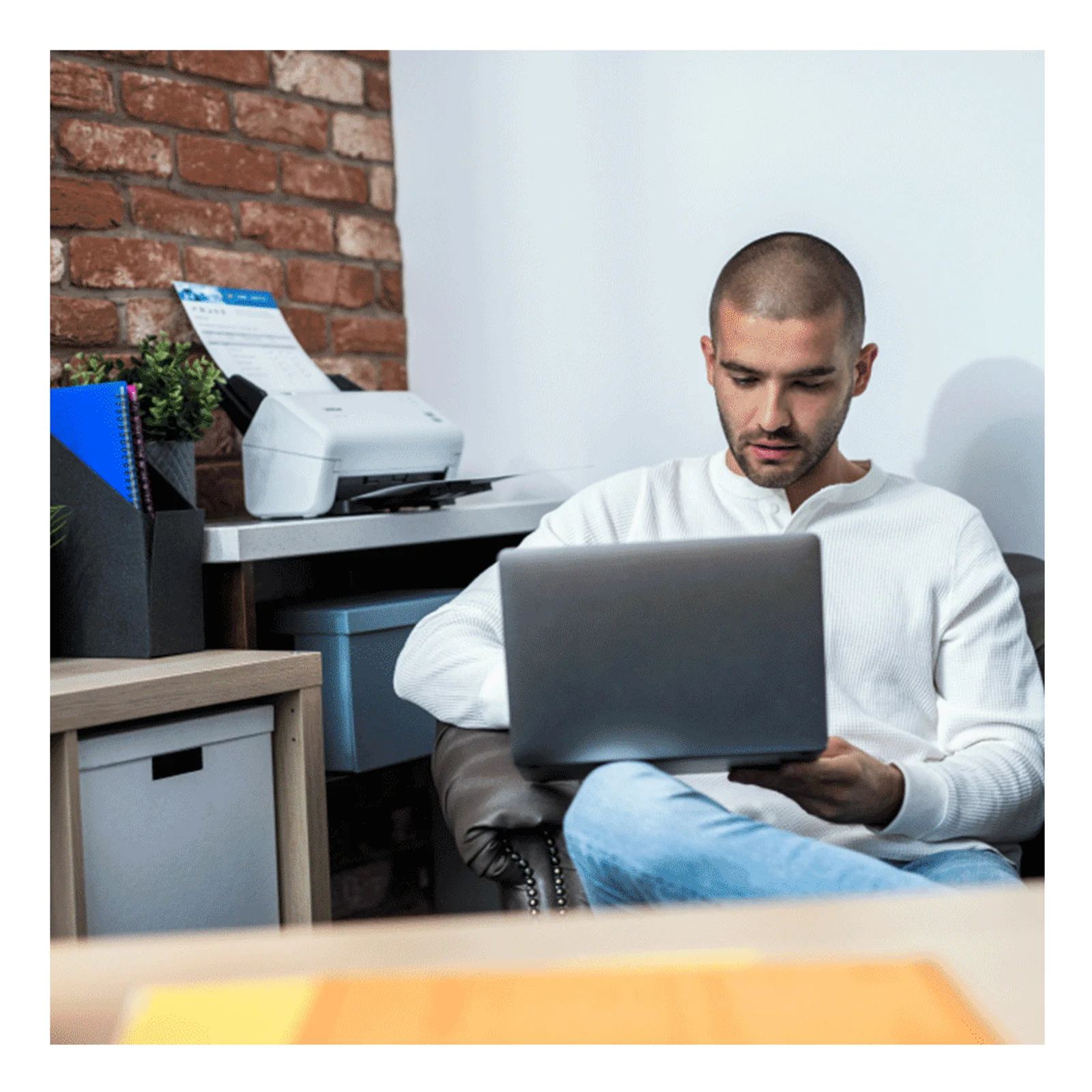 Homme assis travaillant sur un ordinateur portable près du scanner ADS-4100 posé sur un meuble en bois