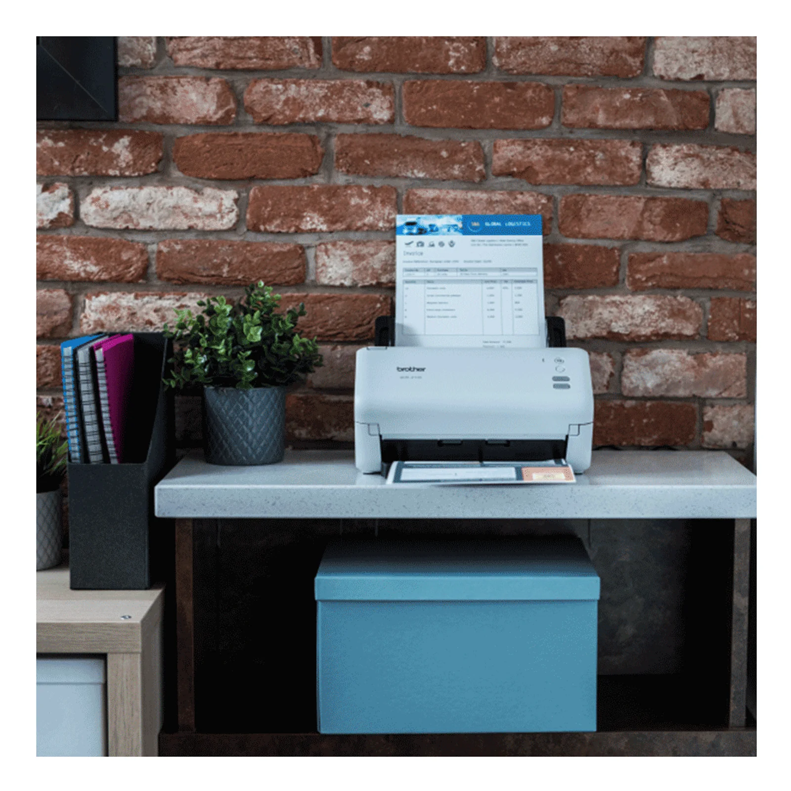 Scanner Brother ADS-4100 sur étagère blanche en environnement de bureau avec mur de briques et classeurs colorés