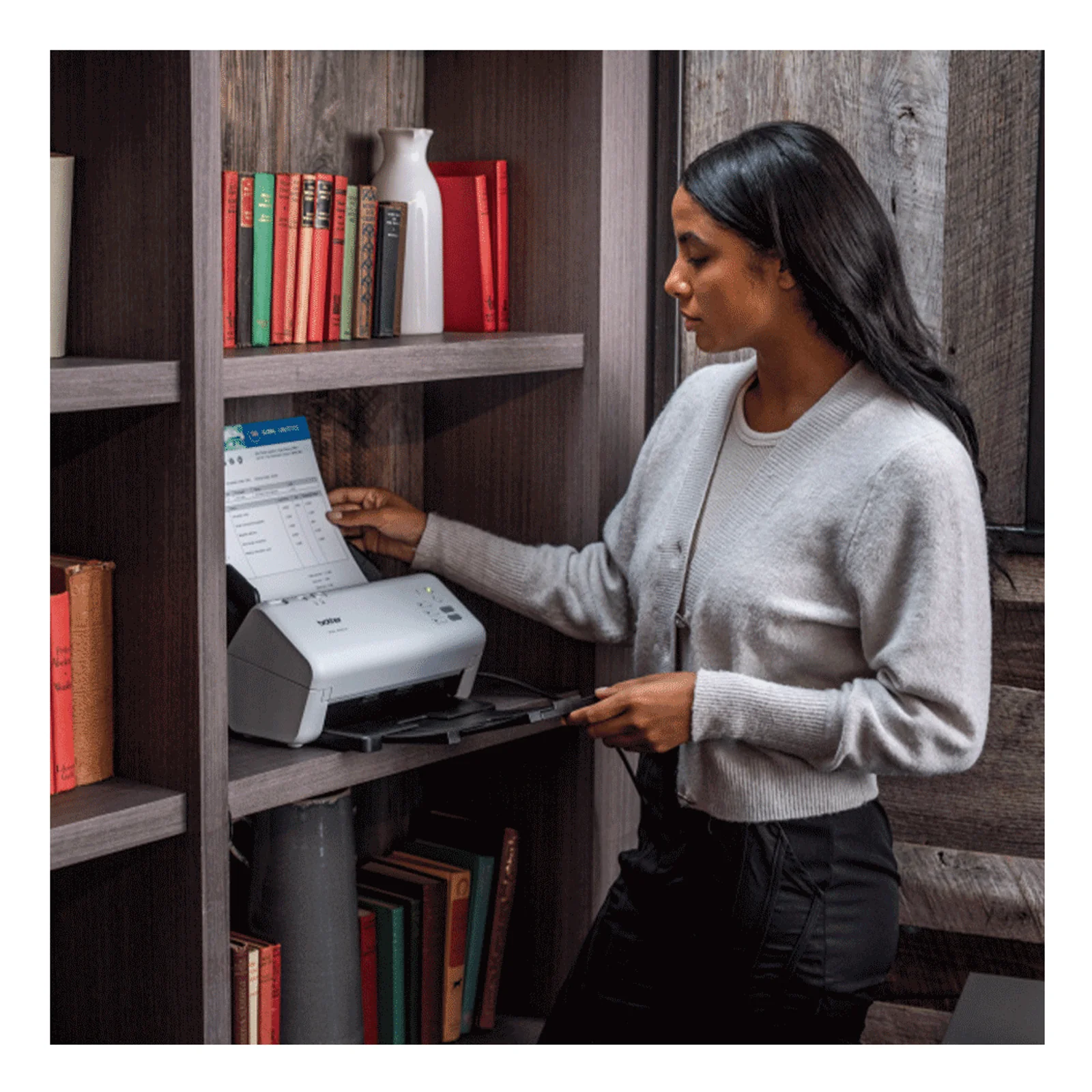 Femme en pull blanc utilisant le scanner Brother ADS-4300N installé sur une étagère murale en bois sombre