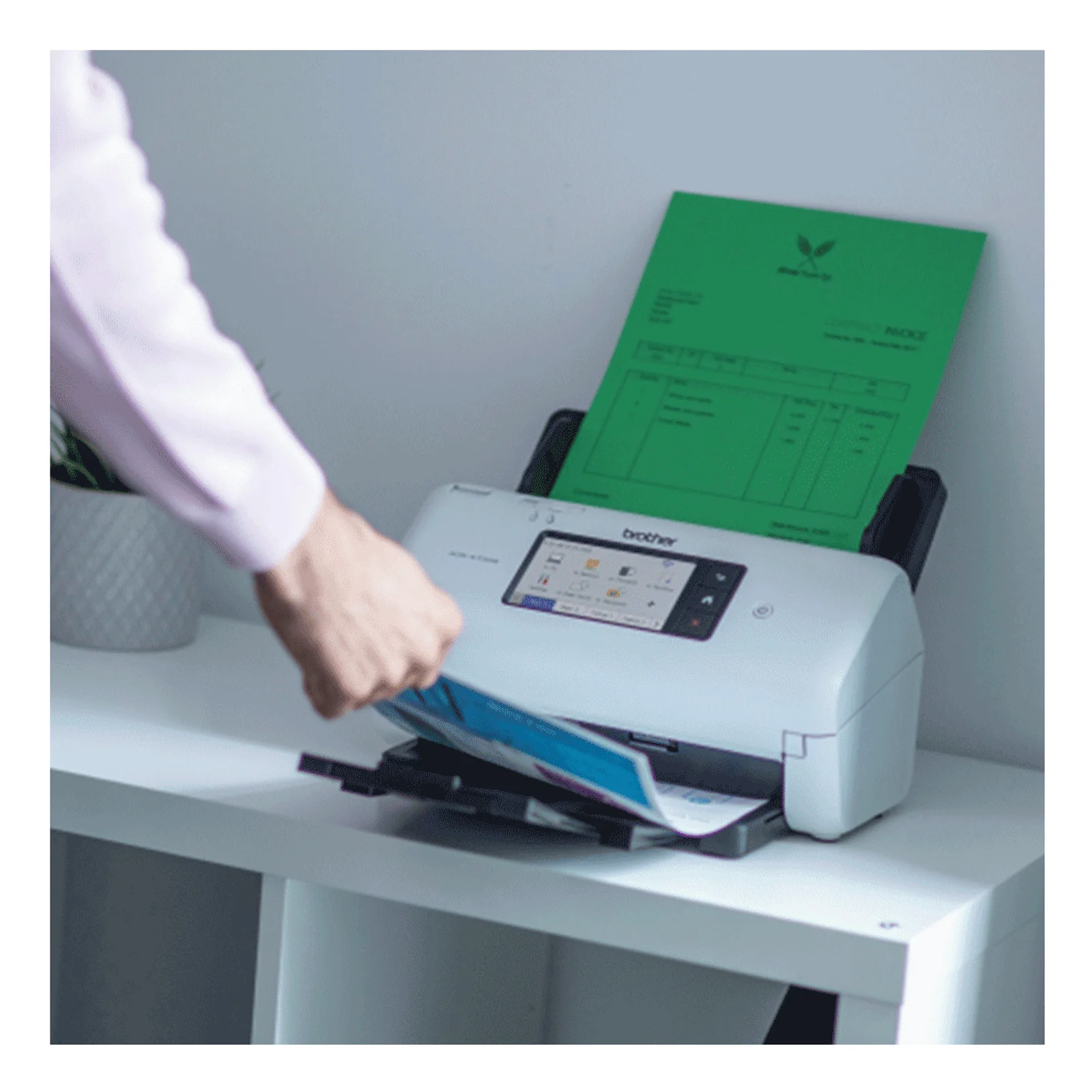 Main retirant des documents du bac de sortie du scanner Brother avec page verte au chargement