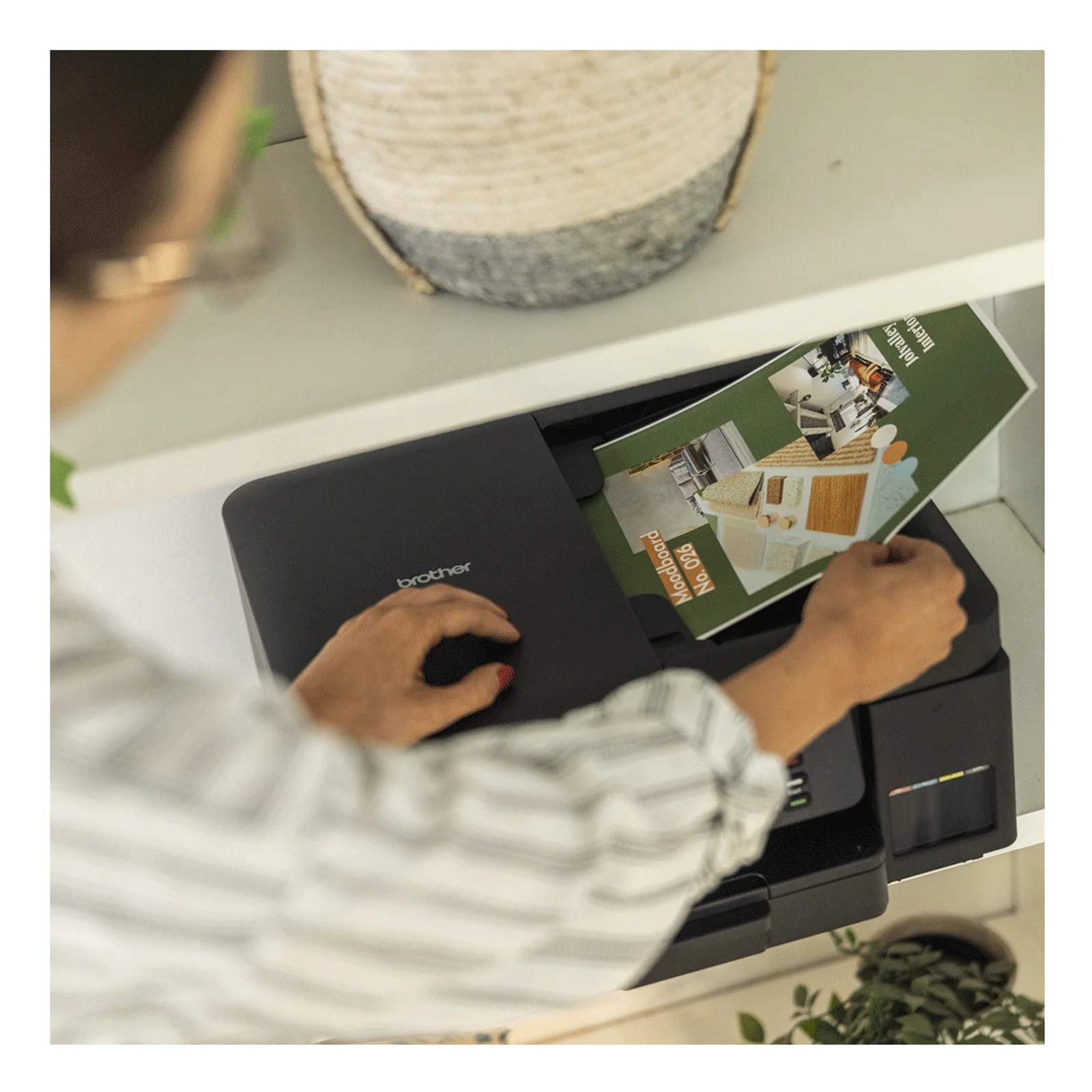 Personne utilisant l'imprimante Brother DCP-T780DW posée sur un meuble blanc avec un magazine couleur en sortie