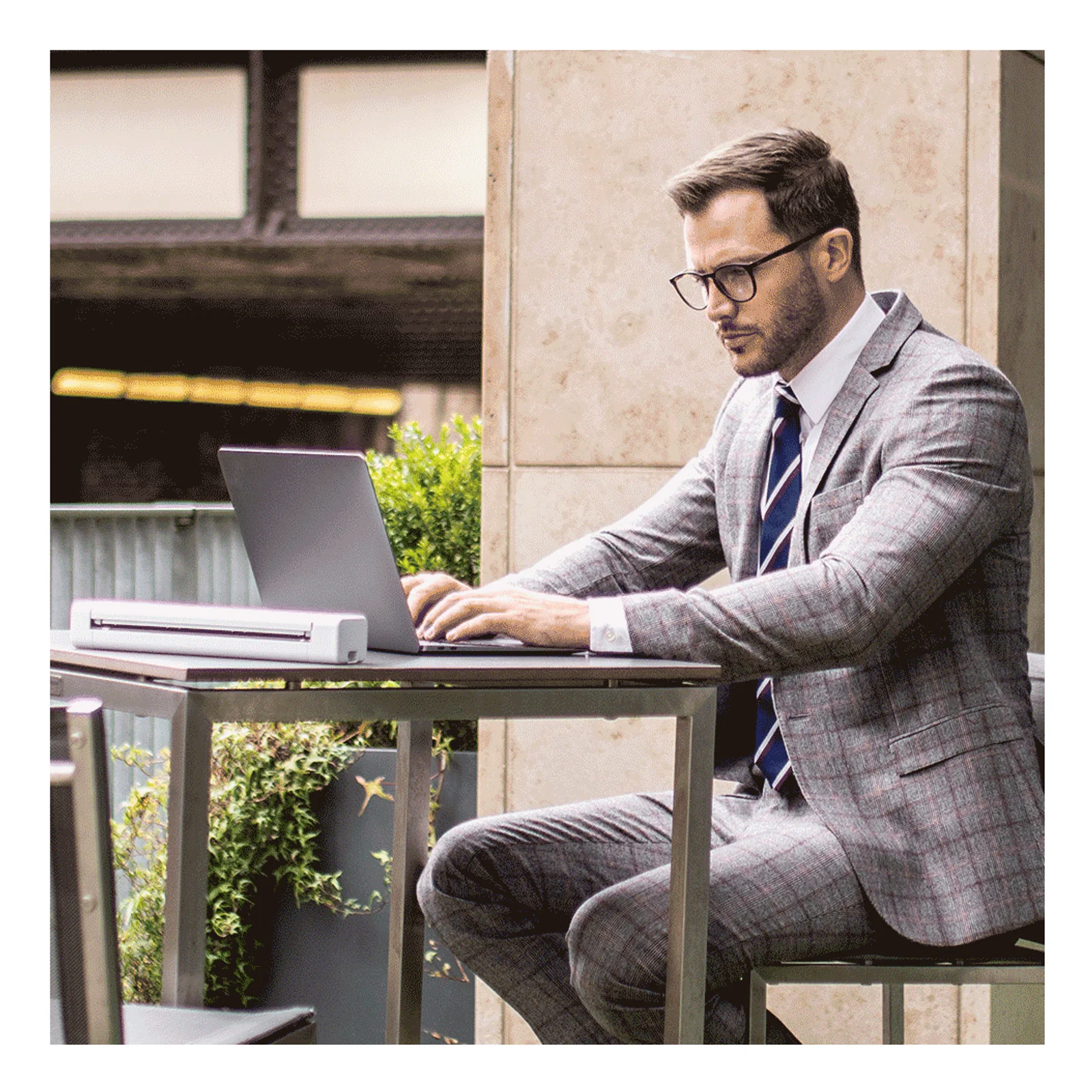 Homme en costume utilisant son ordinateur portable en terrasse avec scanner Brother DS-640 posé sur la table