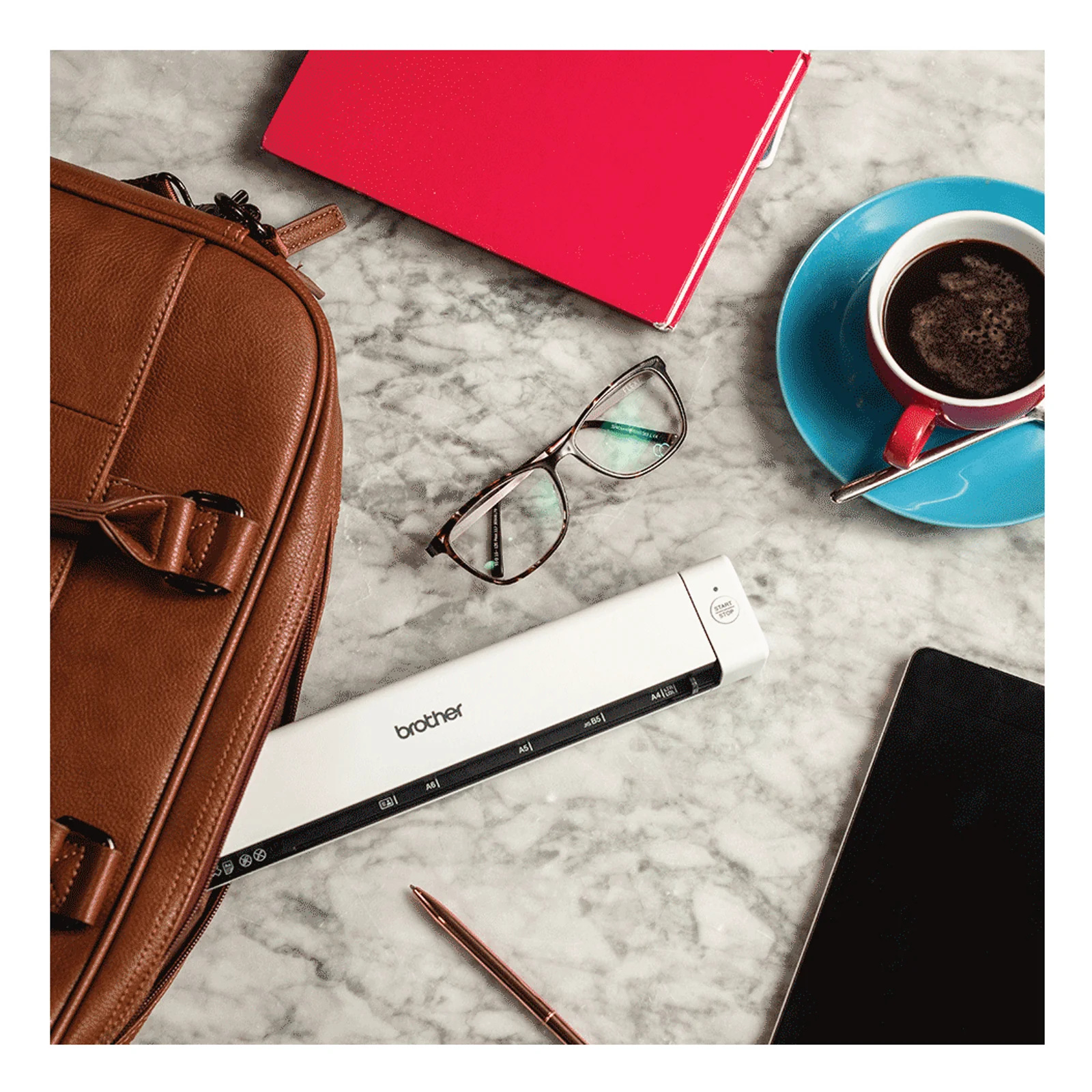 Scanner Brother DS-640 sur surface en marbre près d'une sacoche cuir, lunettes et tasse de café bleue