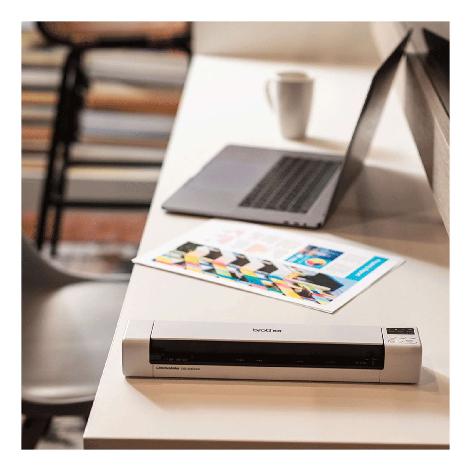 Scanner Brother DS-940DW posé sur un bureau à côté d'un ordinateur portable et d'une feuille imprimée