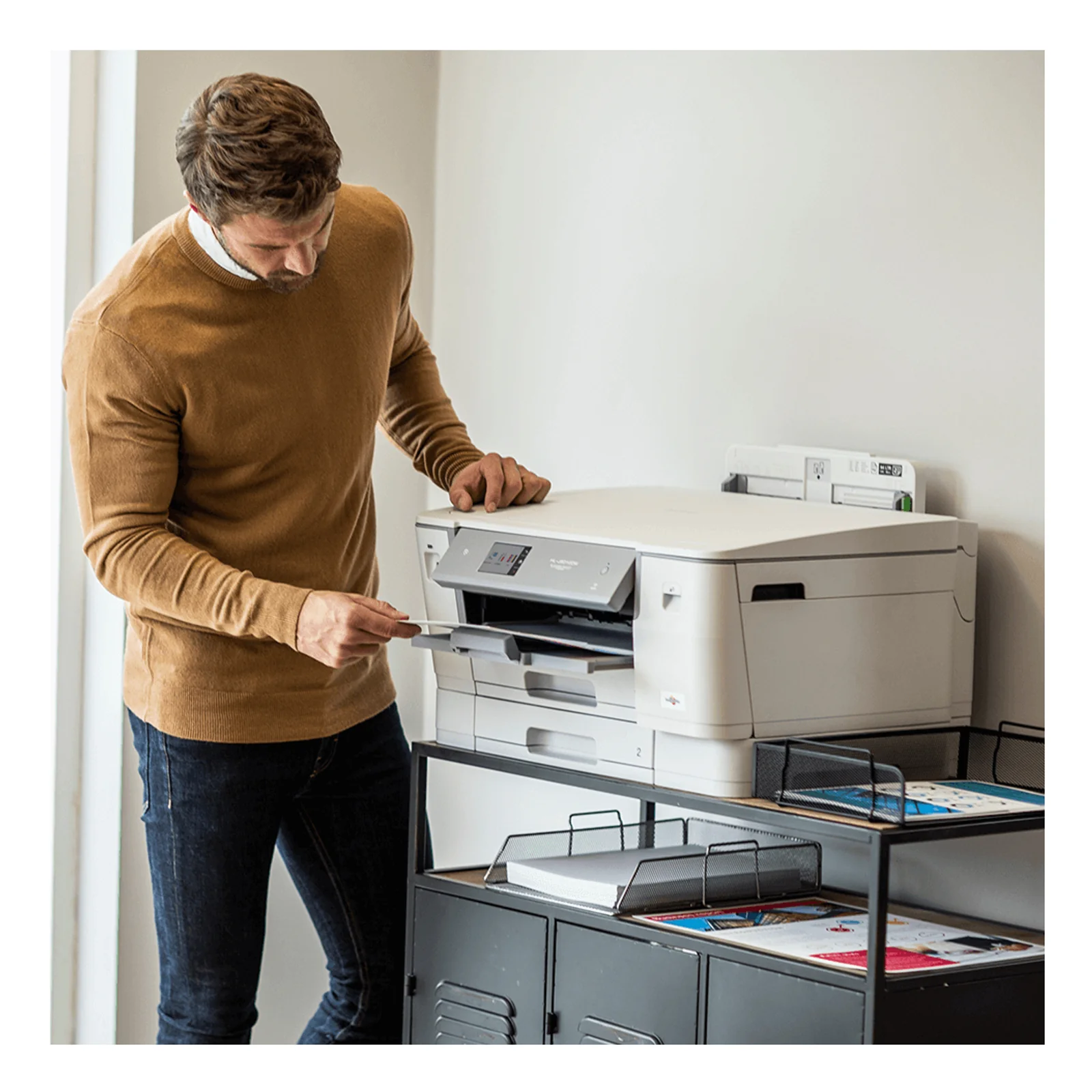 Homme en pull camel debout devant l'imprimante Brother HL-J6010DW posée sur une desserte de bureau