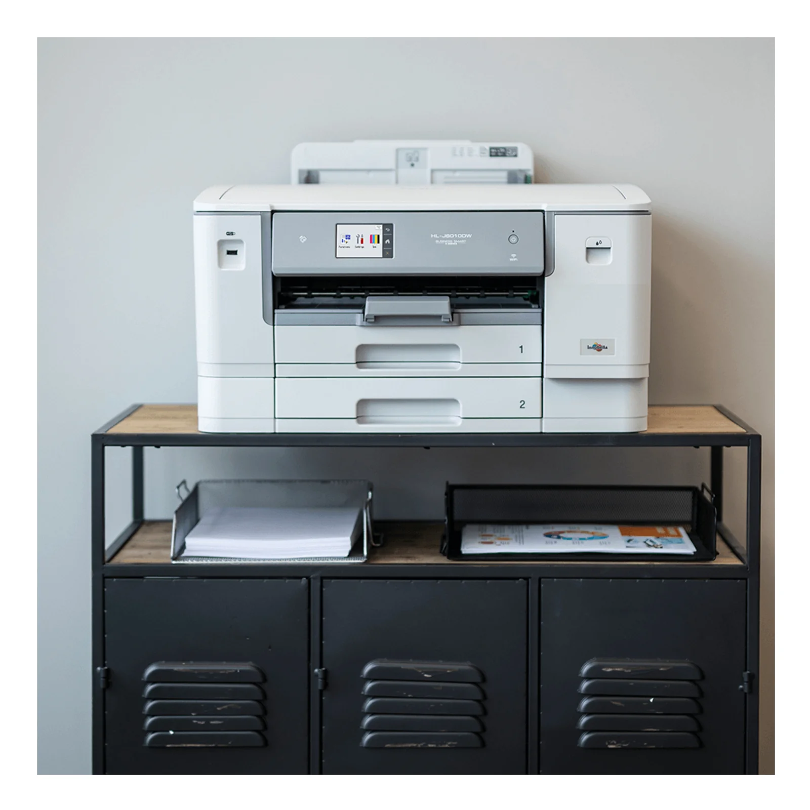 Imprimante Brother HL-J6010DW posée sur une console en bois et métal noir devant un mur gris clair