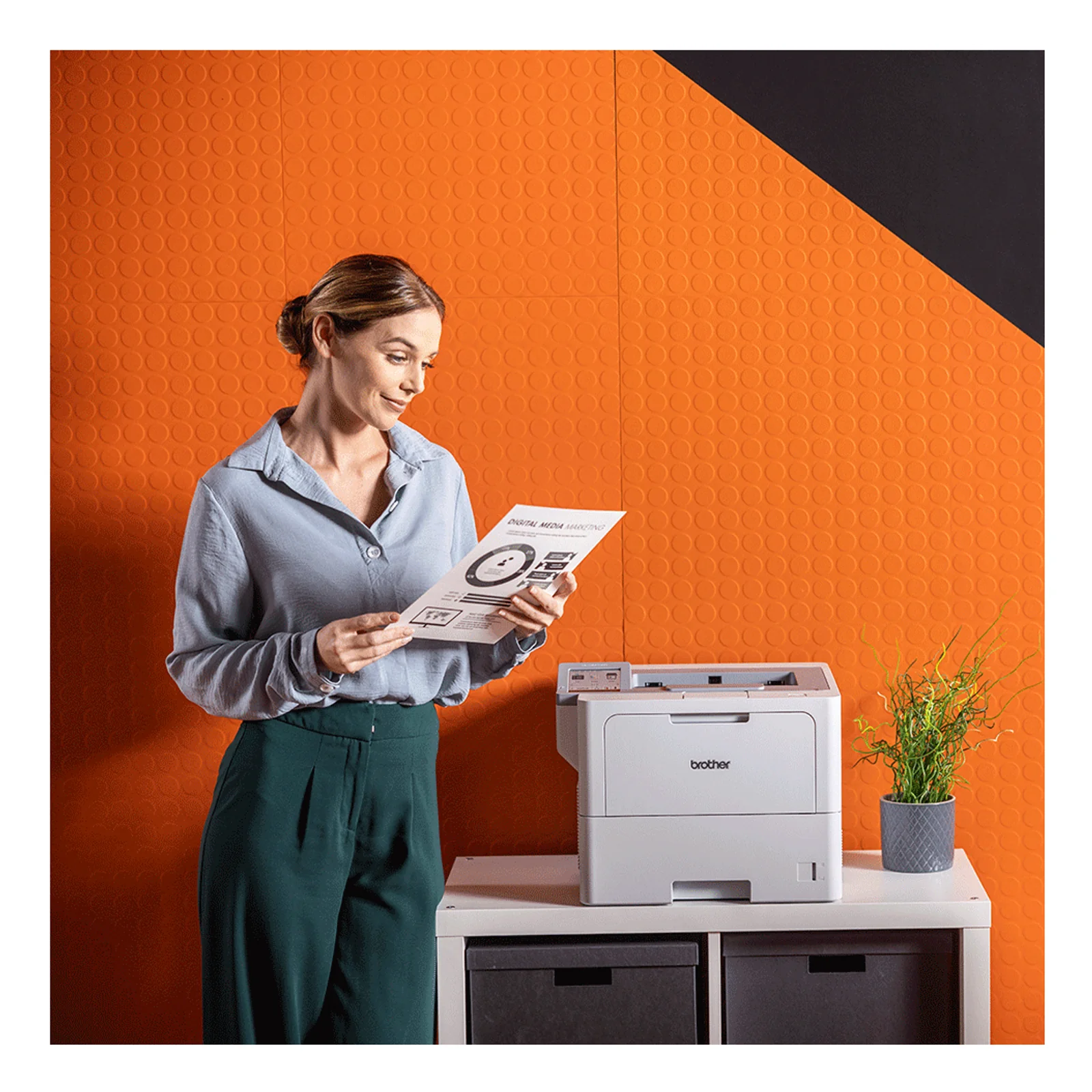 Femme en chemise bleue lisant une page imprimée à côté de la Brother HL-L6410DN sur fond orange