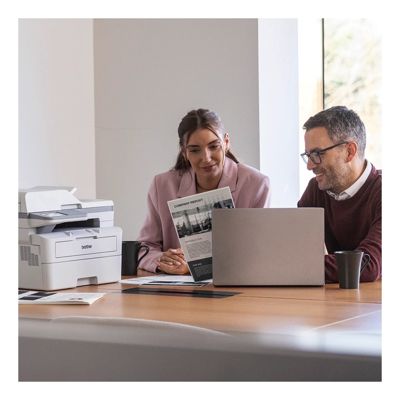 Couple en réunion autour d'un ordinateur portable avec multifonction MFC-L2960DW posé sur le bureau à gauche