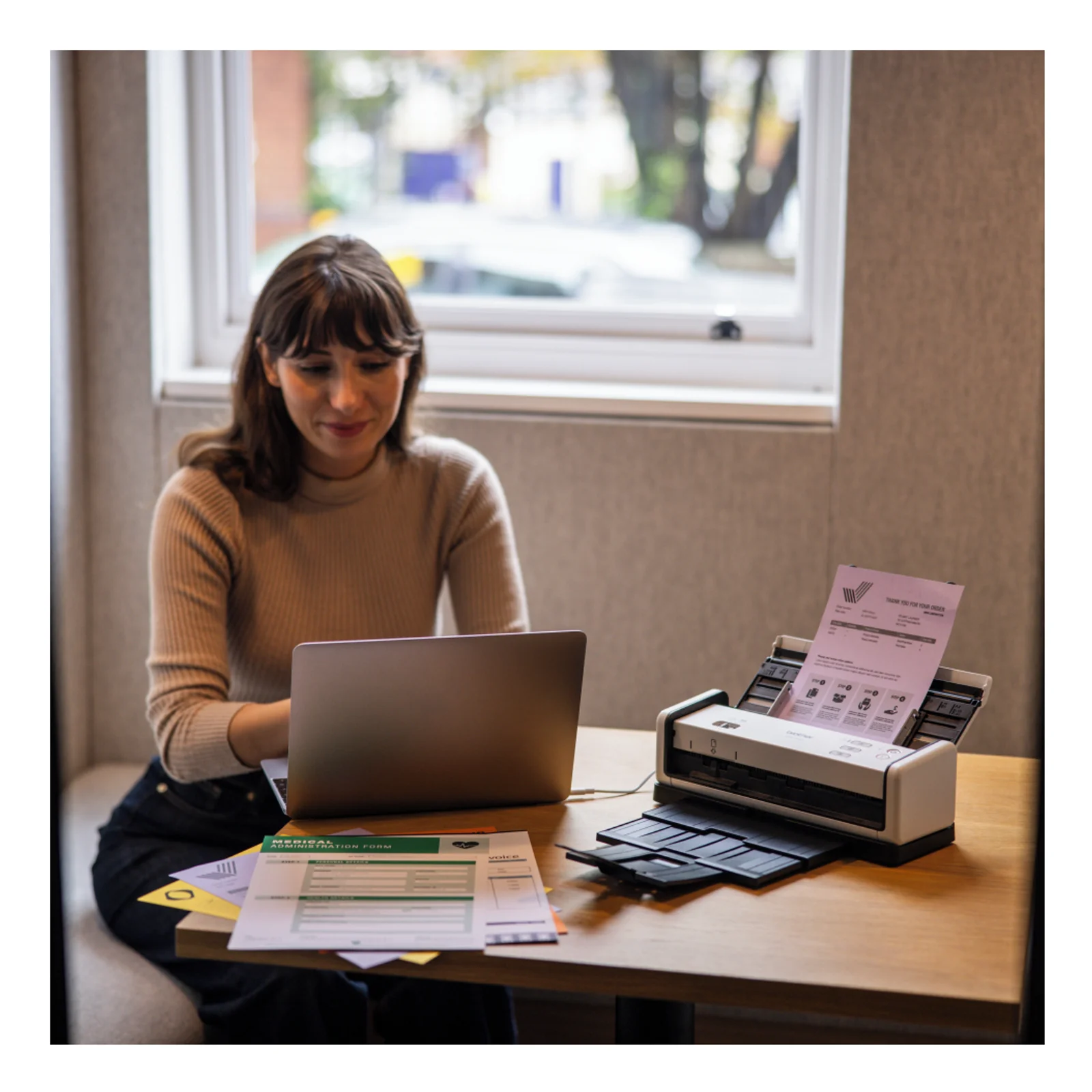 Femme assise à un bureau utilisant un ordinateur portable à côté d'un scanner Brother ADS équipé du bac de sortie OT-1001C