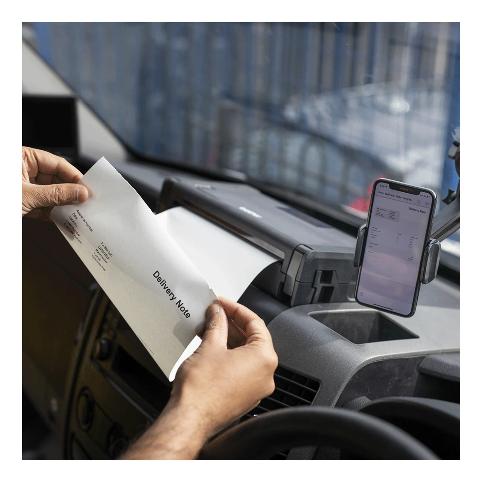 Mise en situation, technicien en cabine de camion saisissant un bon de livraison sortant de la PJ-883 fixée sur le tableau de bord, smartphone à droite