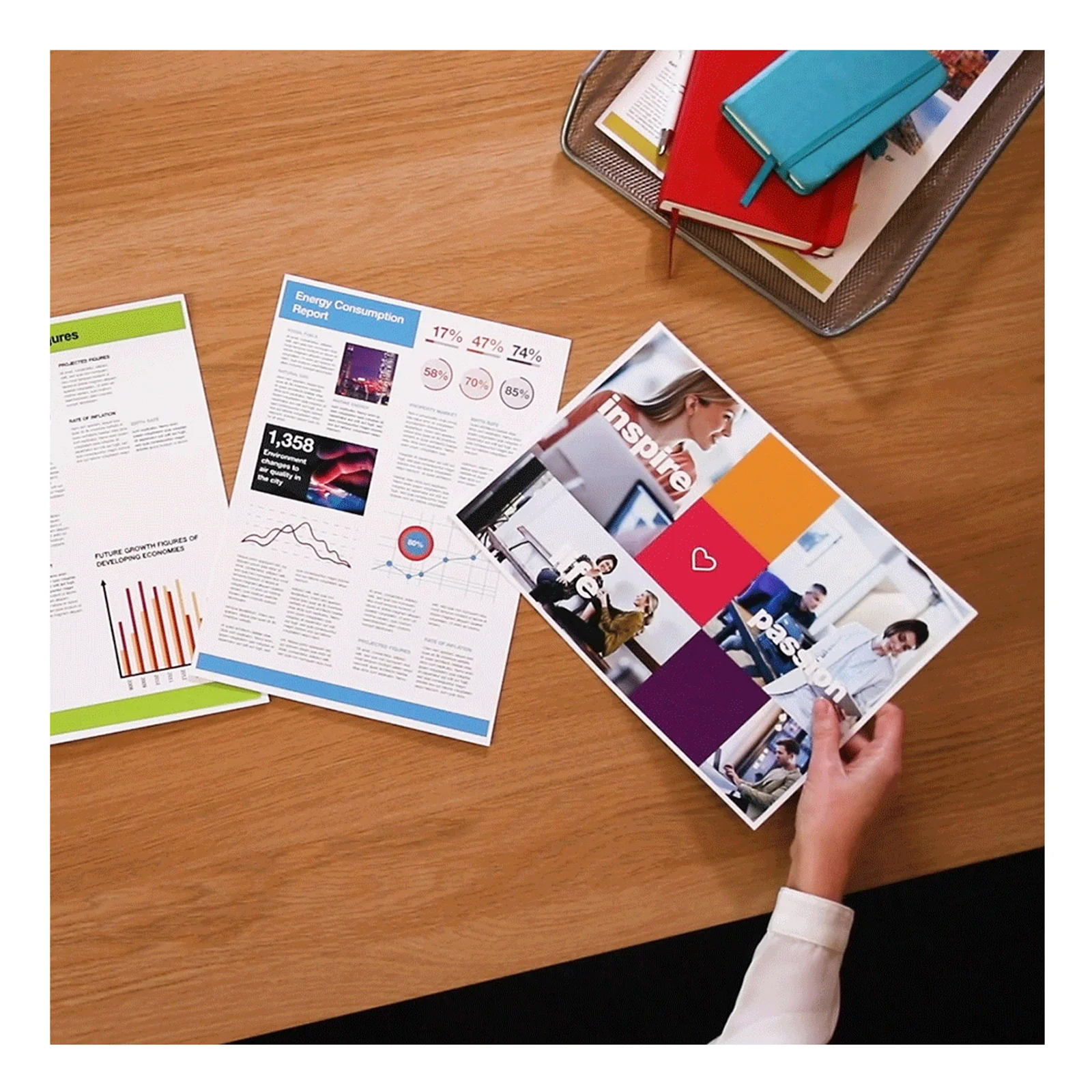 Documents et brochures imprimés en couleur posés sur un bureau en bois clair avec carnet bleu