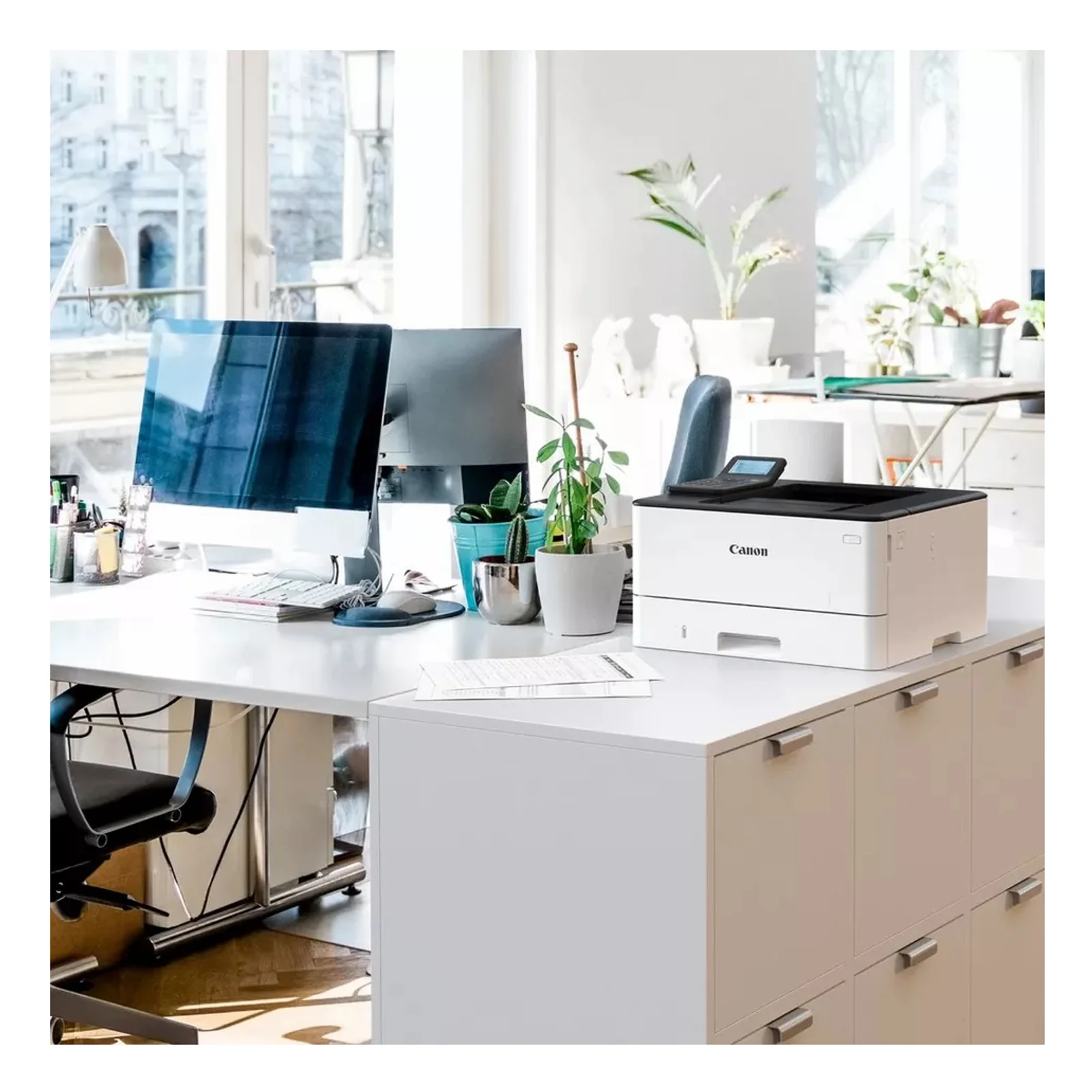 Canon LBP246dw II posée sur un caisson dans un bureau lumineux avec écrans et plantes