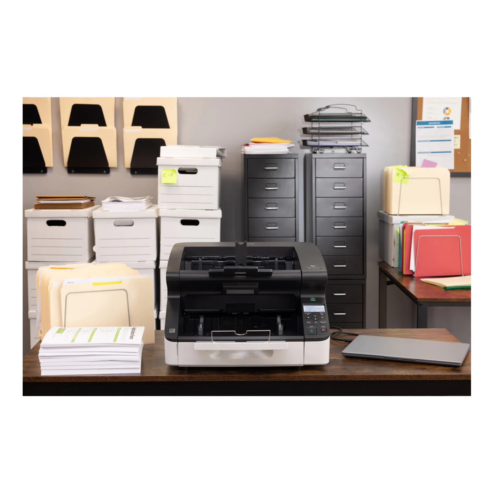 Mise en situation du DR-G2110 dans un bureau avec opérateur travaillant à l'arrière-plan et boîtes d'archivage stockées