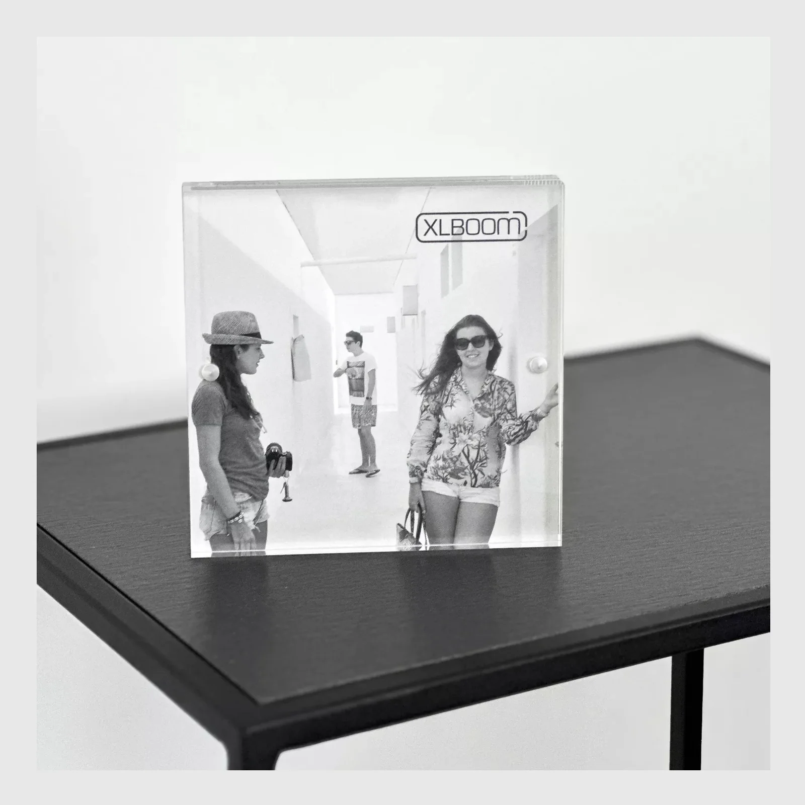 Cadre acrylique transparent XLBoom 13x13 cm posé sur une table noire avec photo