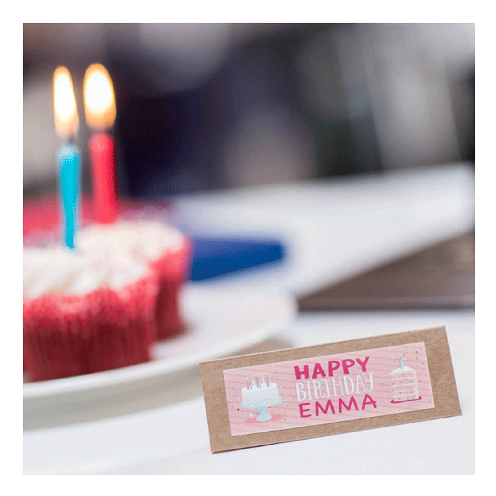 Chevalet d'anniversaire Happy Birthday Emma posé devant un cupcake rouge avec bougies