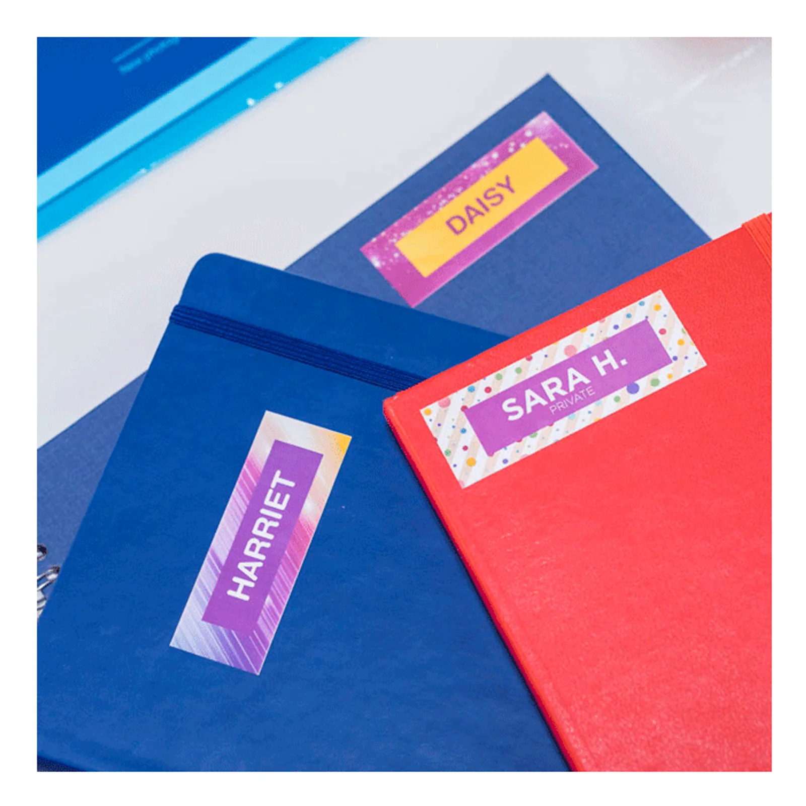 Cahiers et classeurs colorés portant des étiquettes nominatives Daisy Harriet et Sara H.