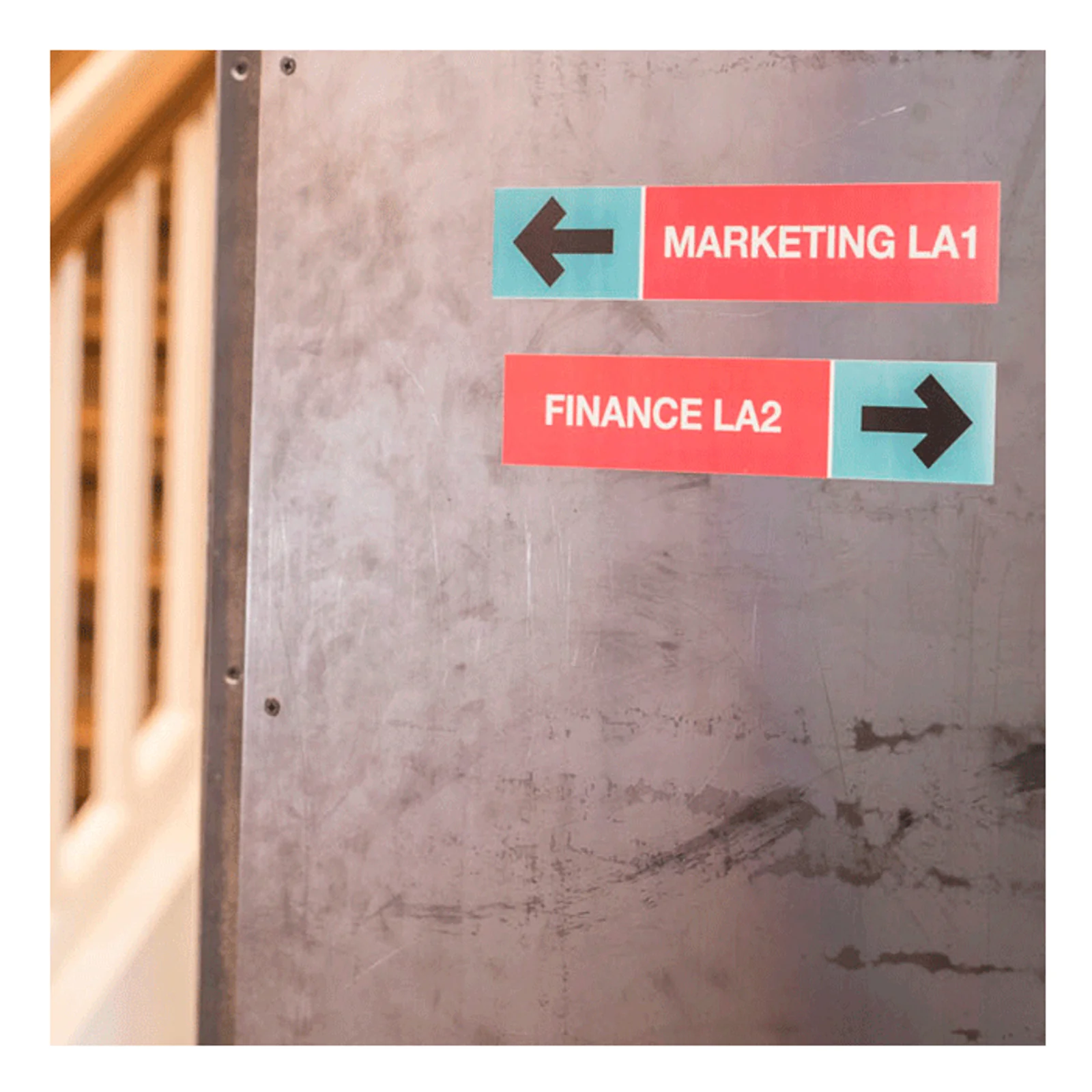 Panneaux directionnels Marketing LA1 et Finance LA2 collés sur une cloison métallique grise