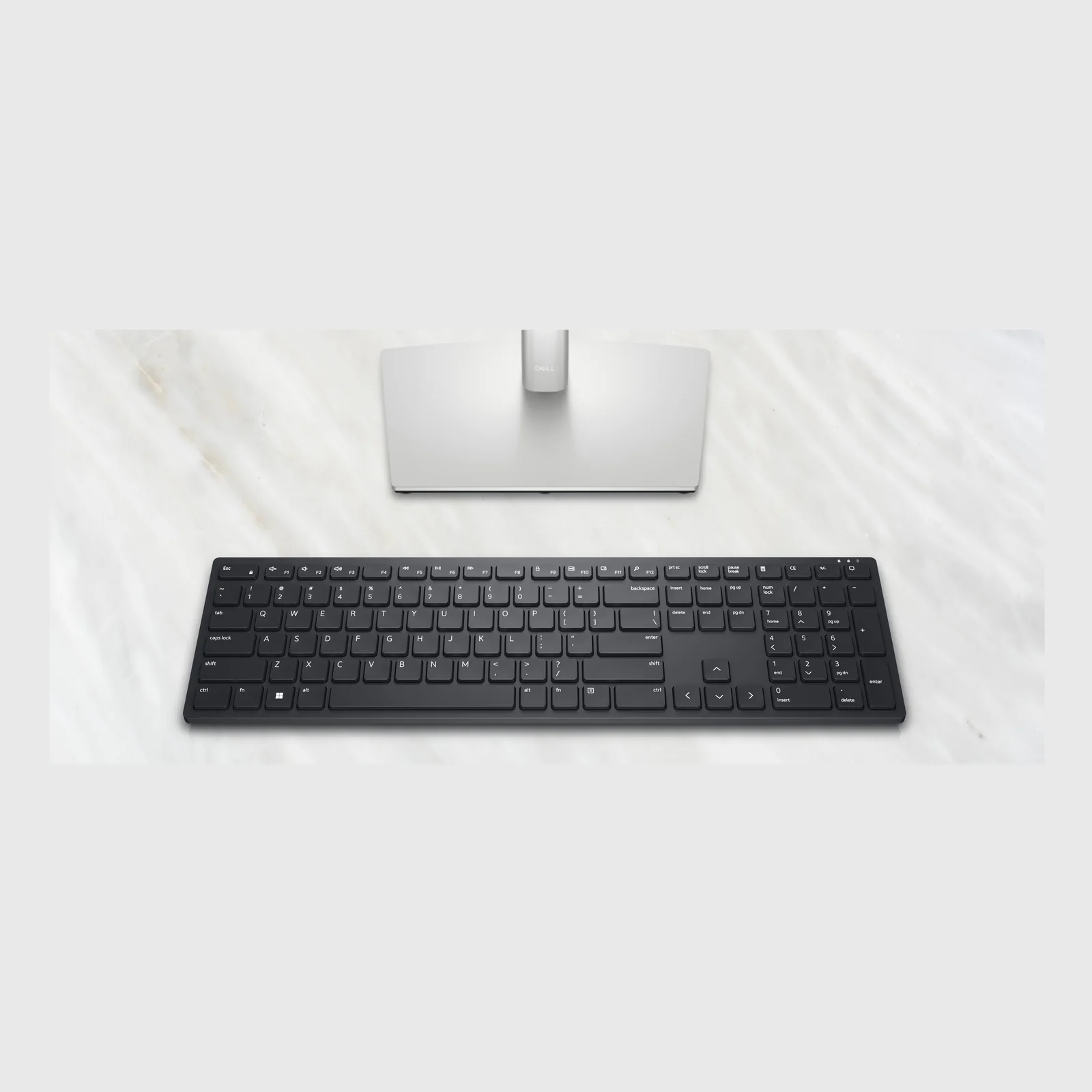 Vue zénithale du clavier posé devant un pied de moniteur Dell sur une surface en marbre clair