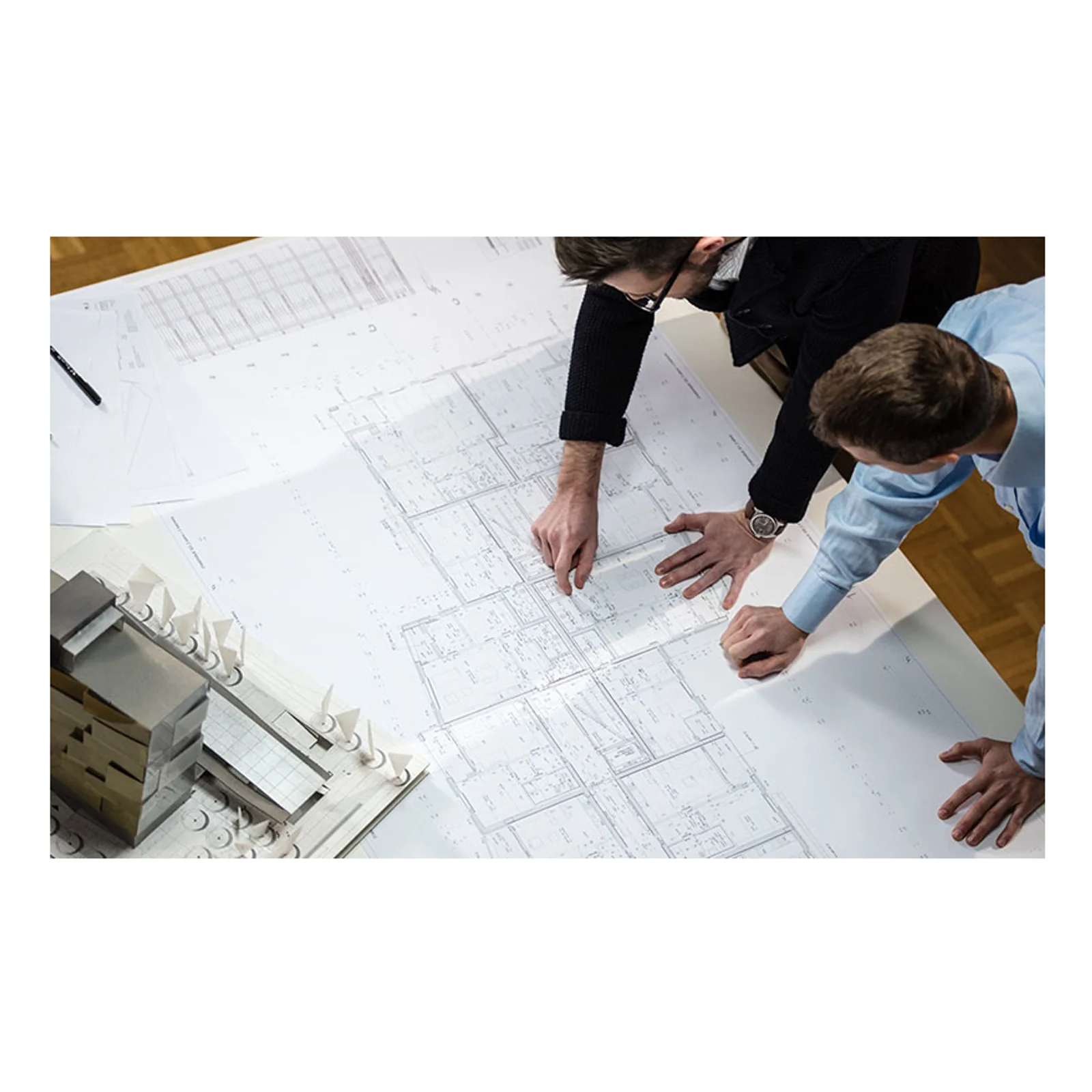 Vue en plongée de deux personnes consultant des plans architecturaux imprimés grand format à côté d'une maquette de bâtiment