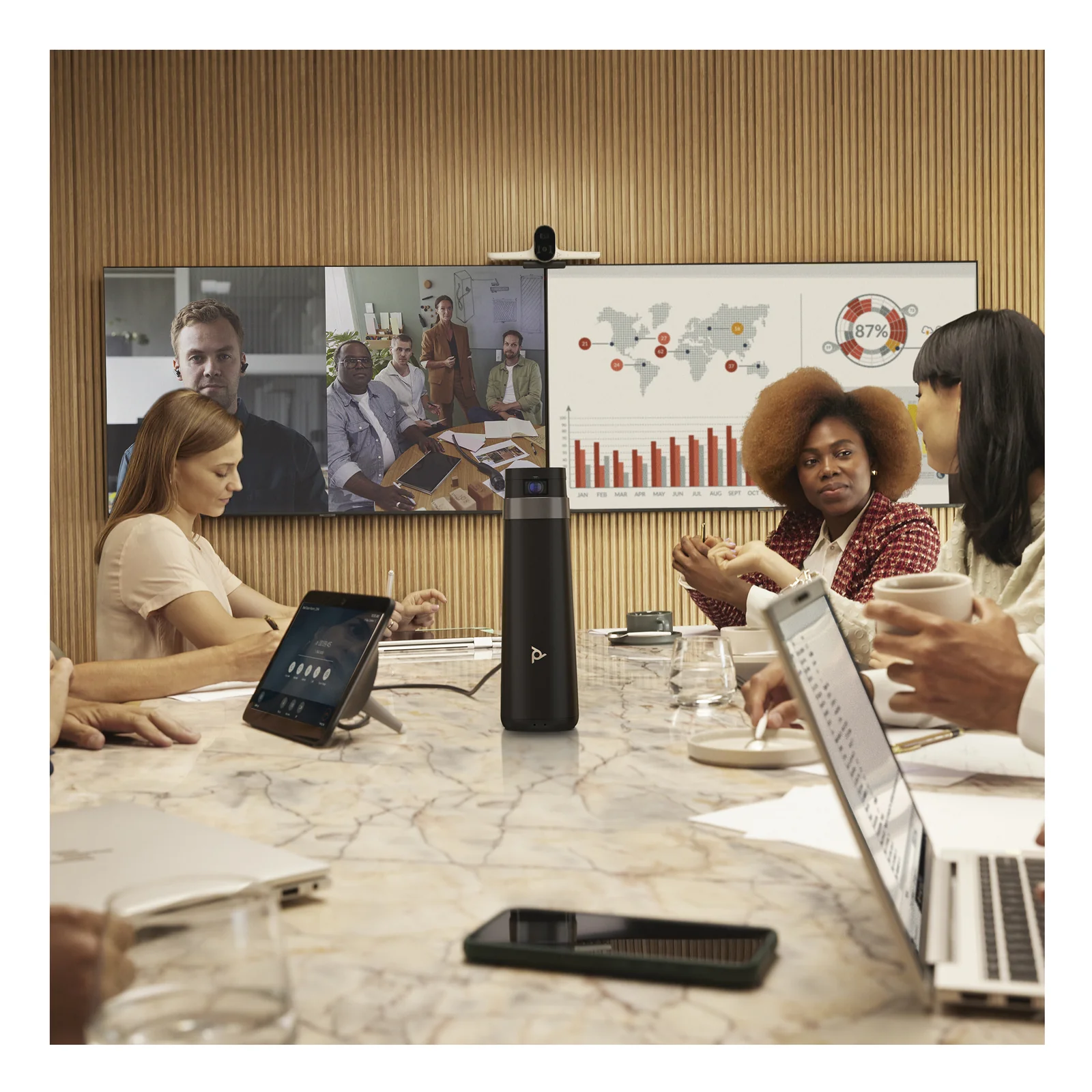Salle de conférence avec système Poly Studio G62 et colonne de microphone, participants en réunion hybride avec écran affichant des visages distants