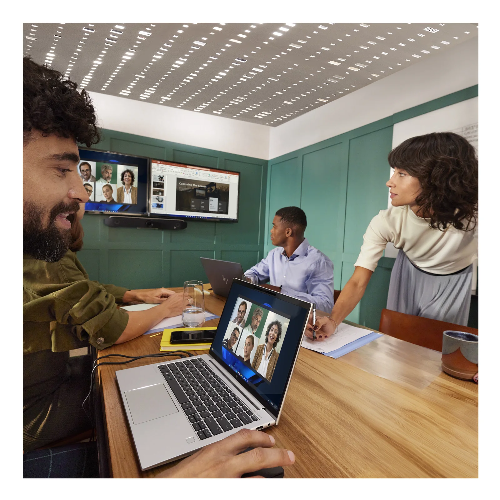 Réunion hybride en petite salle, homme en réunion devant laptop connecté à la Poly Studio V52 installée sur l'écran mural.