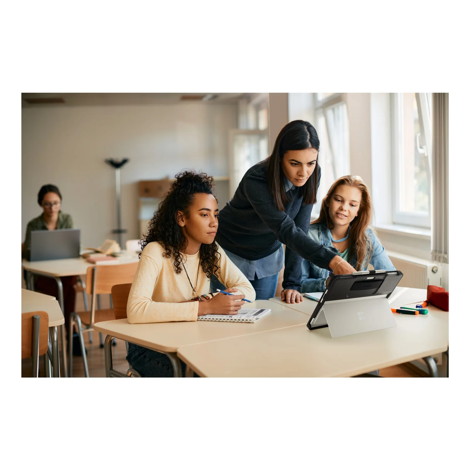 Utilisation en classe, enseignante et deux étudiantes autour d'un Surface Pro en coque