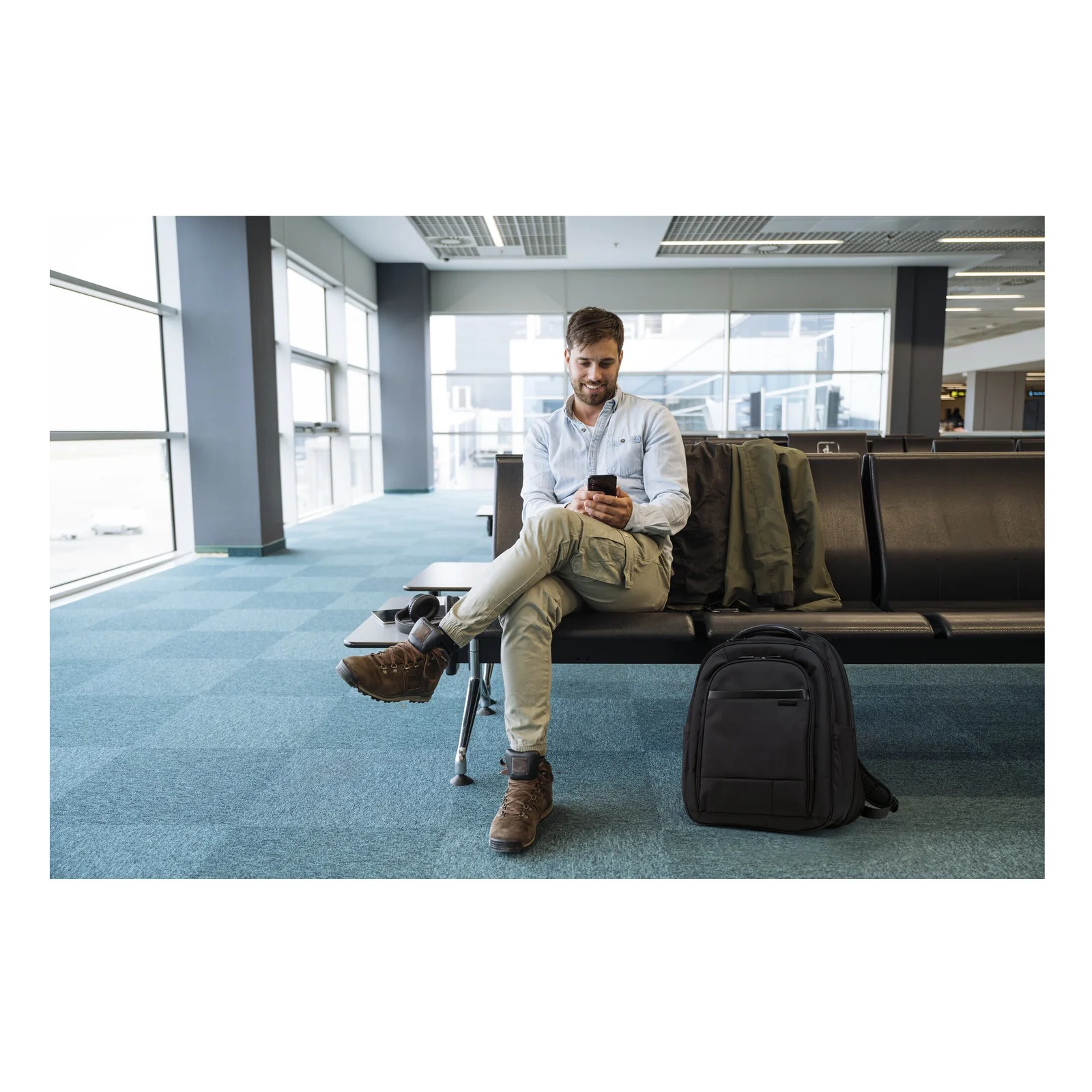 Homme assis dans un aéroport, sac à dos Kensington Contour 2.0 EQ Pro posé à côté de lui