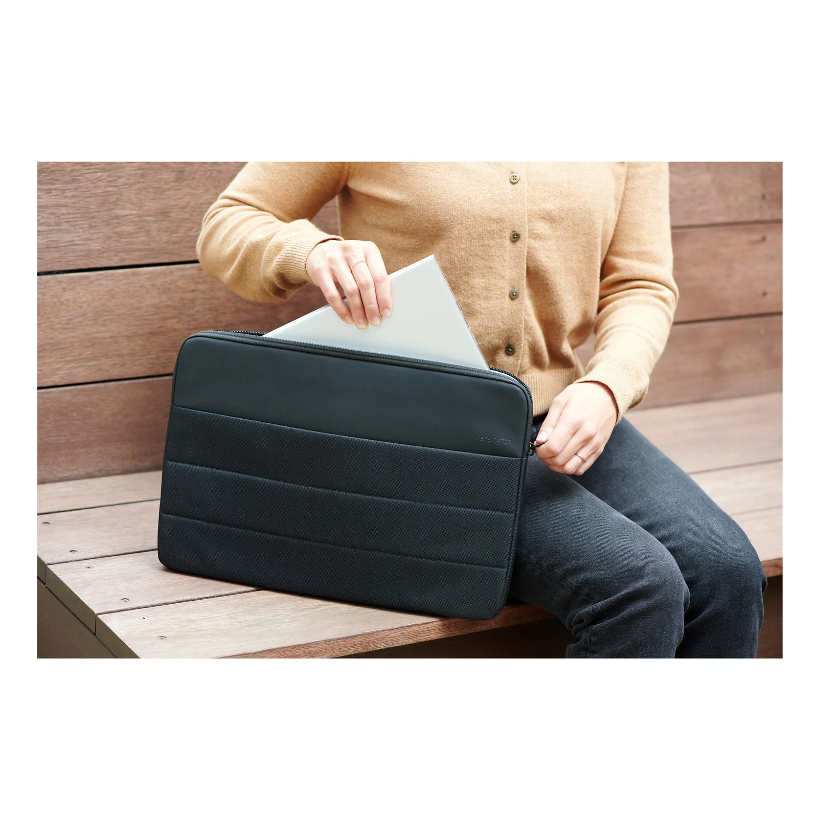 Personne assise sur un banc en extérieur, glisse un ordinateur portable dans une housse vert canard