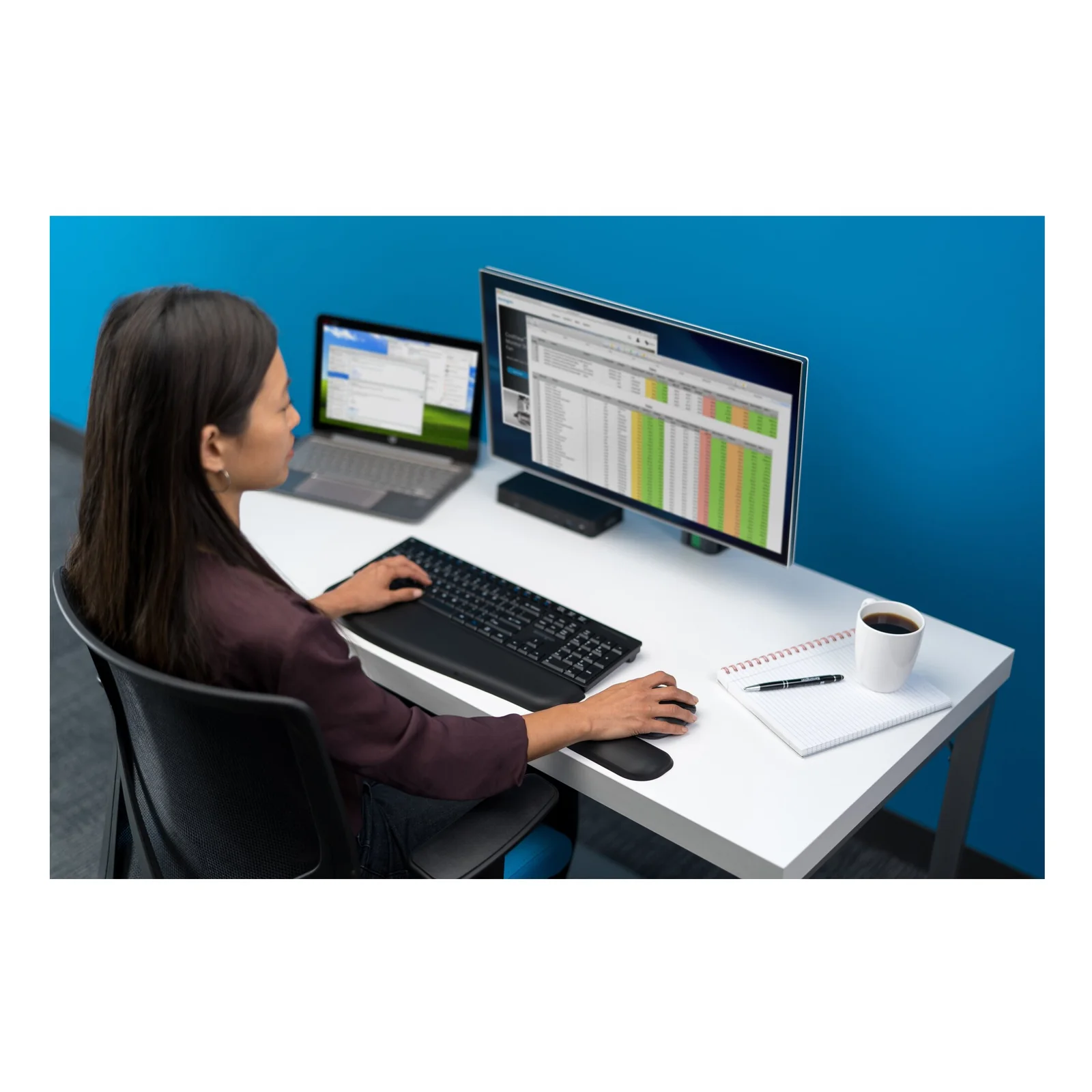 Femme devant double moniteur en open space, setup avec repose-poignet pour souris
