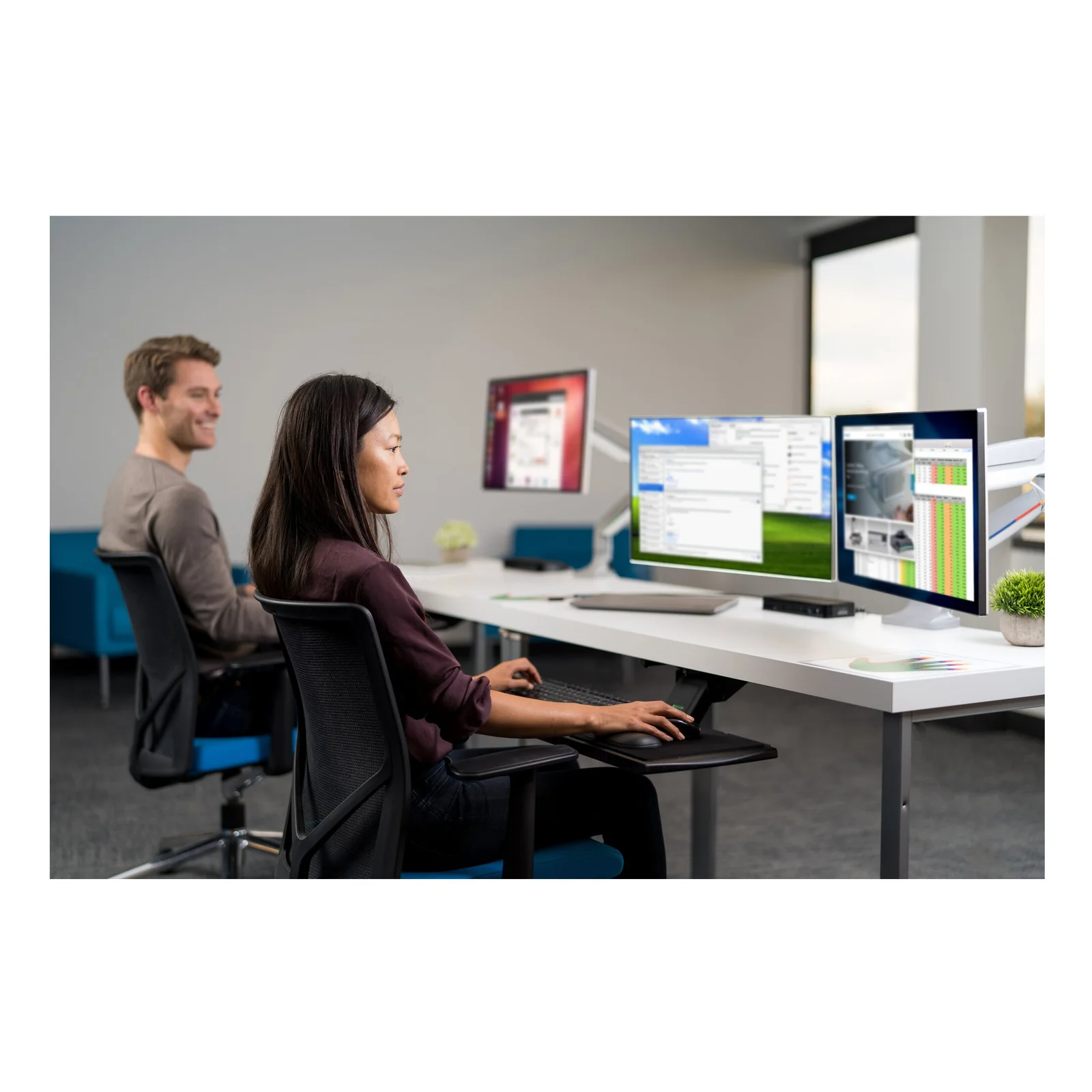 Personne devant configuration multi-écrans en open space, repose-poignet sur bureau