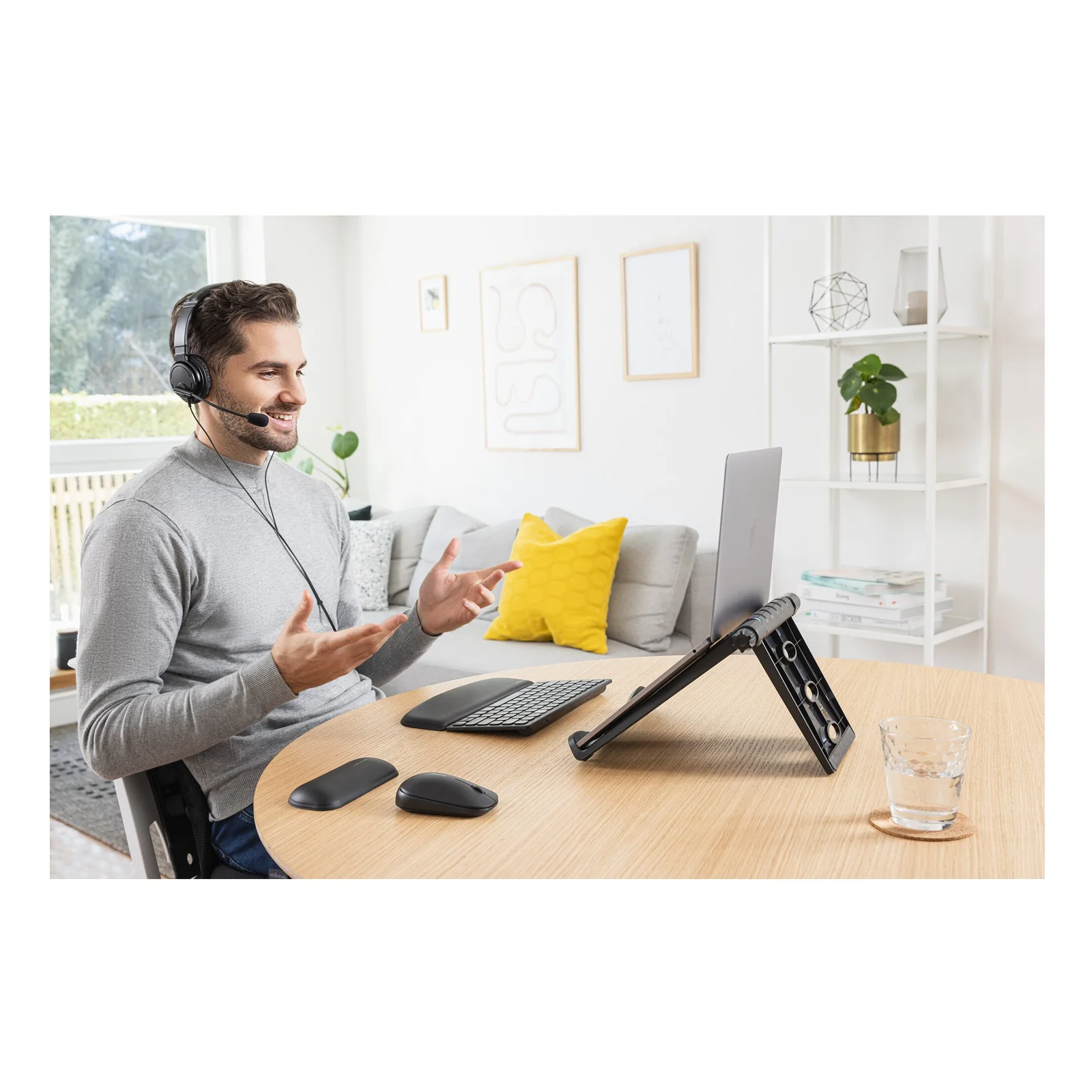 Homme en télétravail avec ordinateur portable sur support réglable, casque audio, bureau blanc