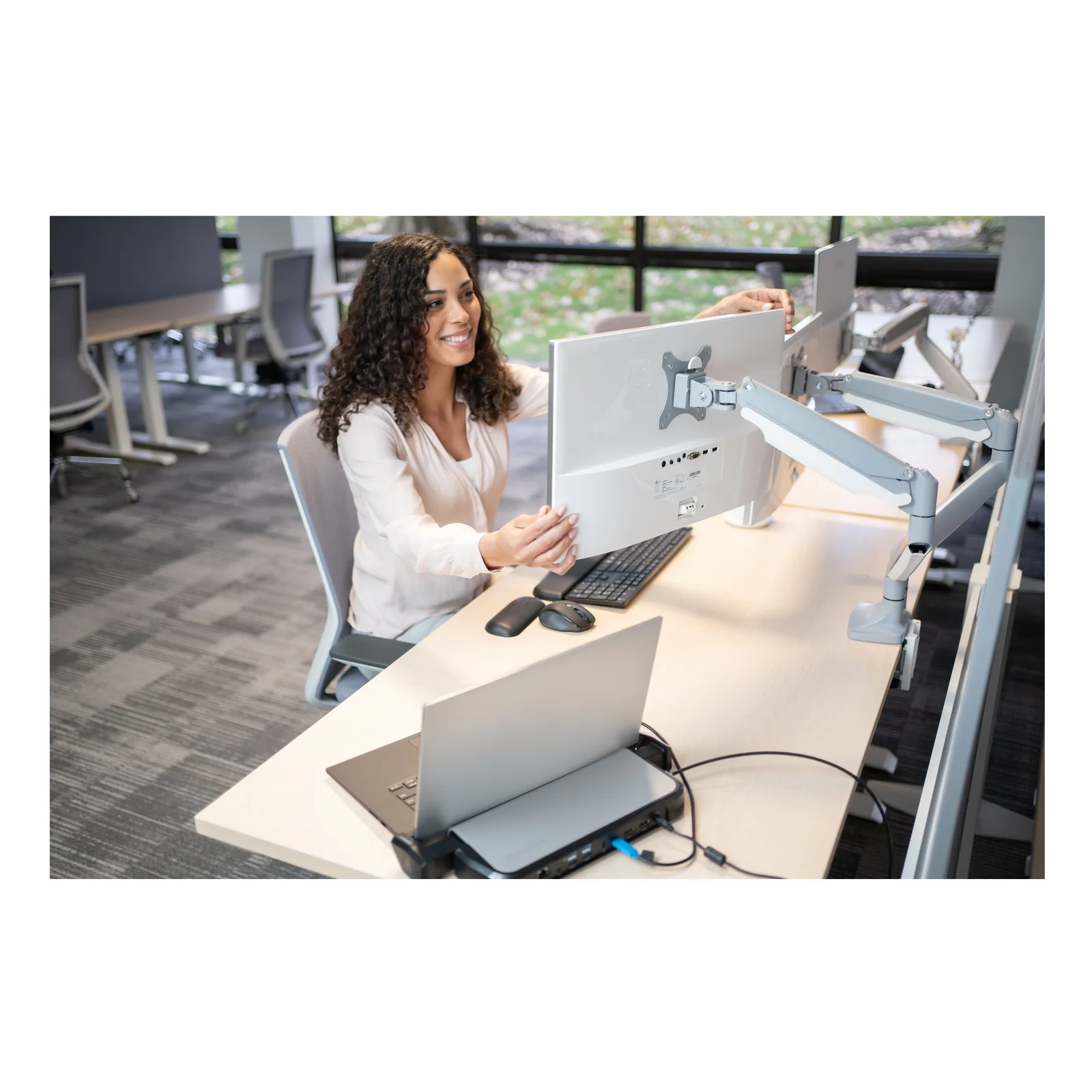 Femme à son bureau ergonomique avec double écran sur bras articulés, open space professionnel