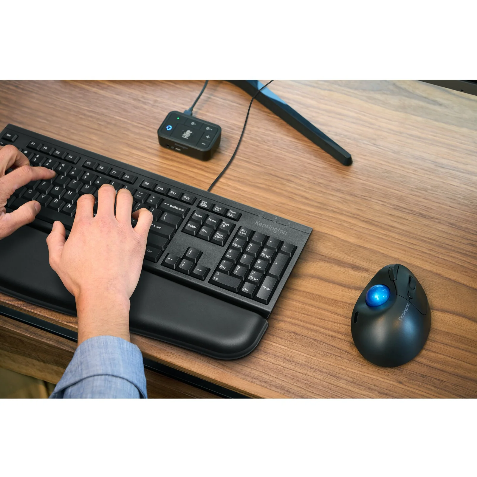 Gros plan sur un trackball et un clavier ergonomique Kensington posés sur un bureau en bois