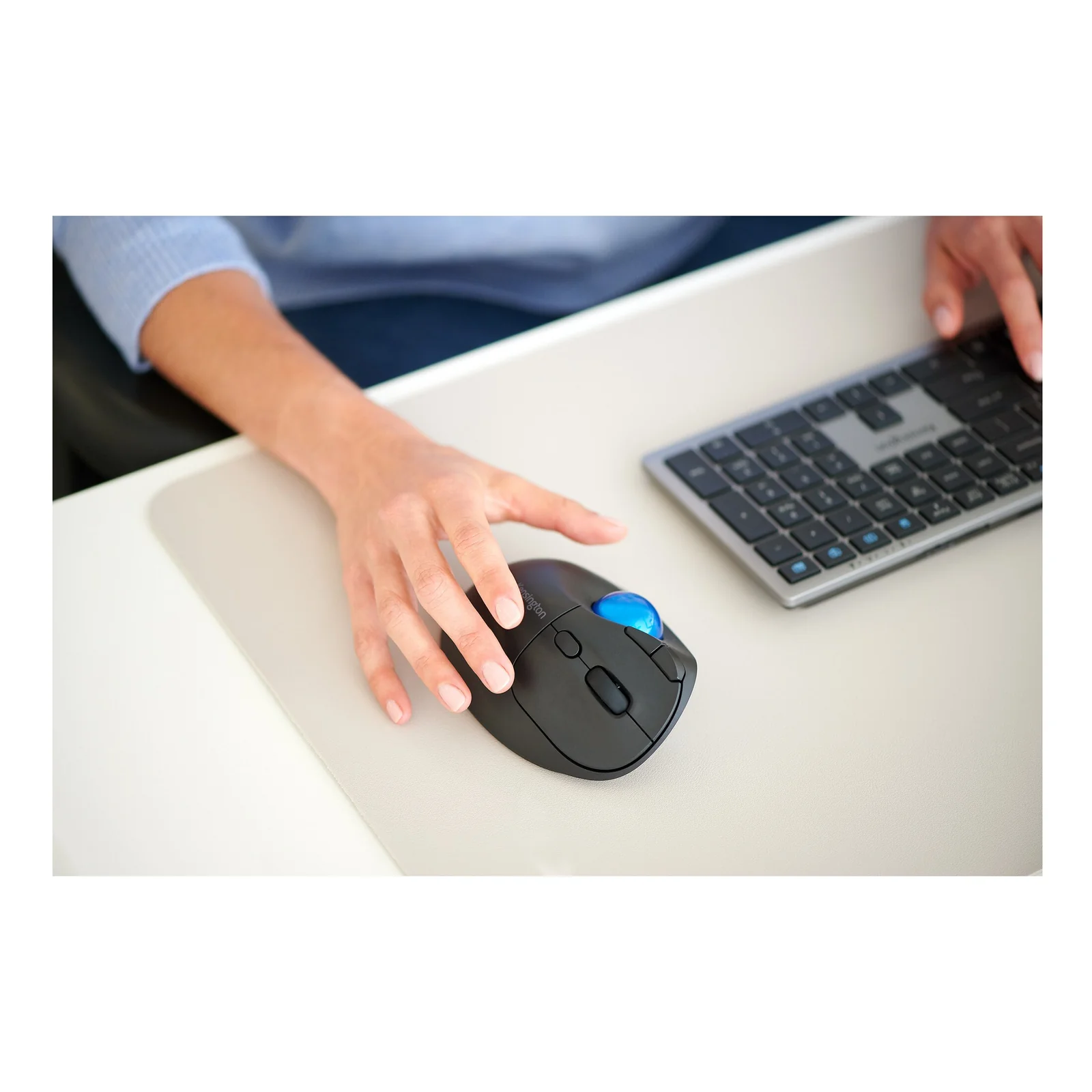 Main sur souris sans fil noire Kensington, KB535 EQ gris visible en fond sur bureau