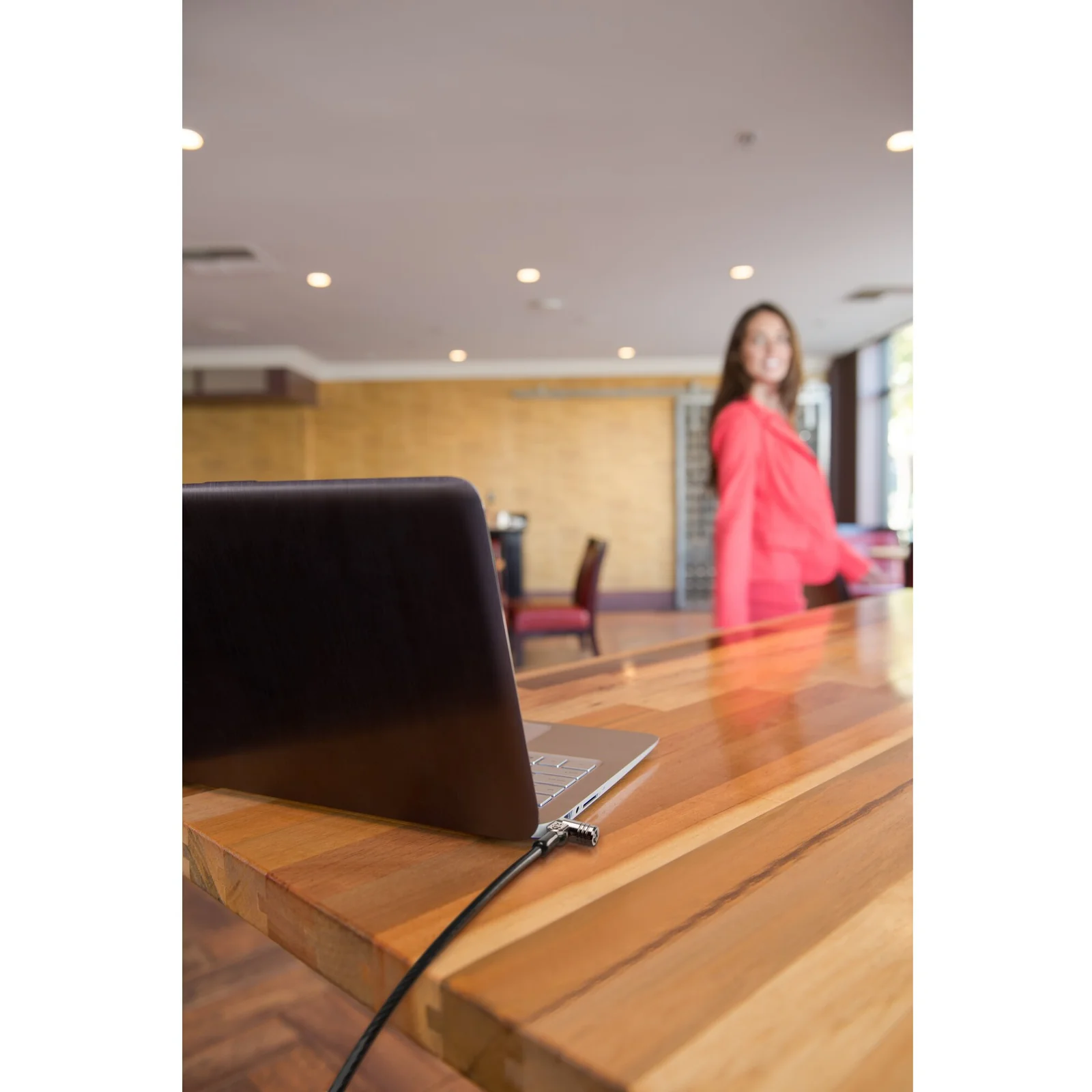 Ordinateur portable sécurisé par un câble Kensington MicroSaver 2.0 posé sur une table de réunion, personne debout en arrière-plan