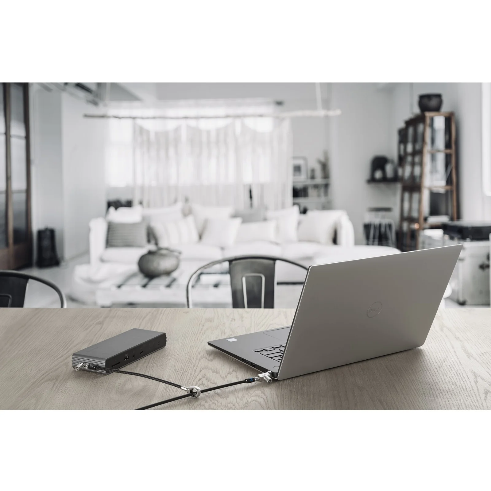 Laptop argenté posé sur une table dans un bureau épuré, câble antivol relié à un appareil externe