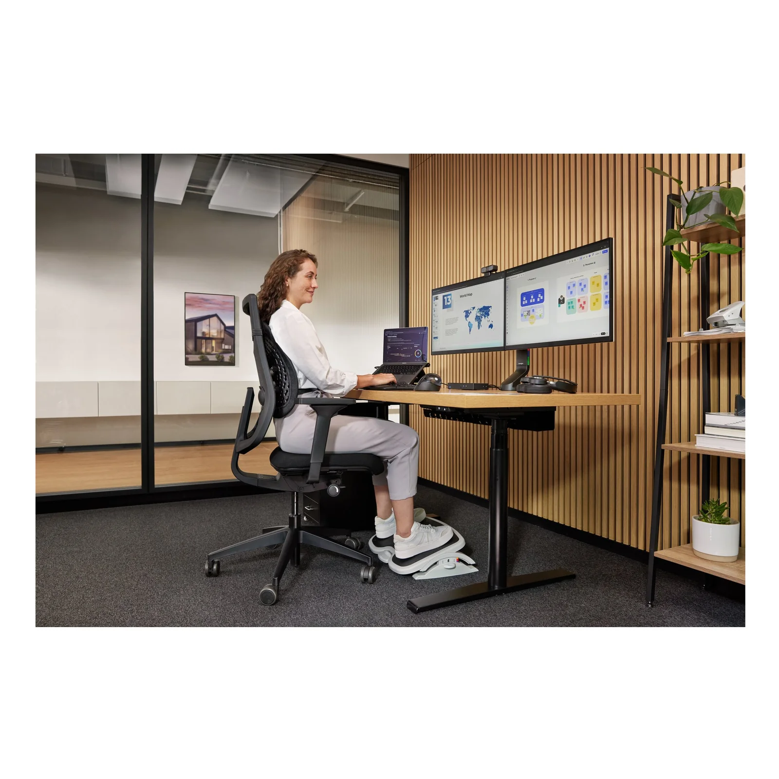 Femme assise à bureau réglable en hauteur avec repose-pied, double écran