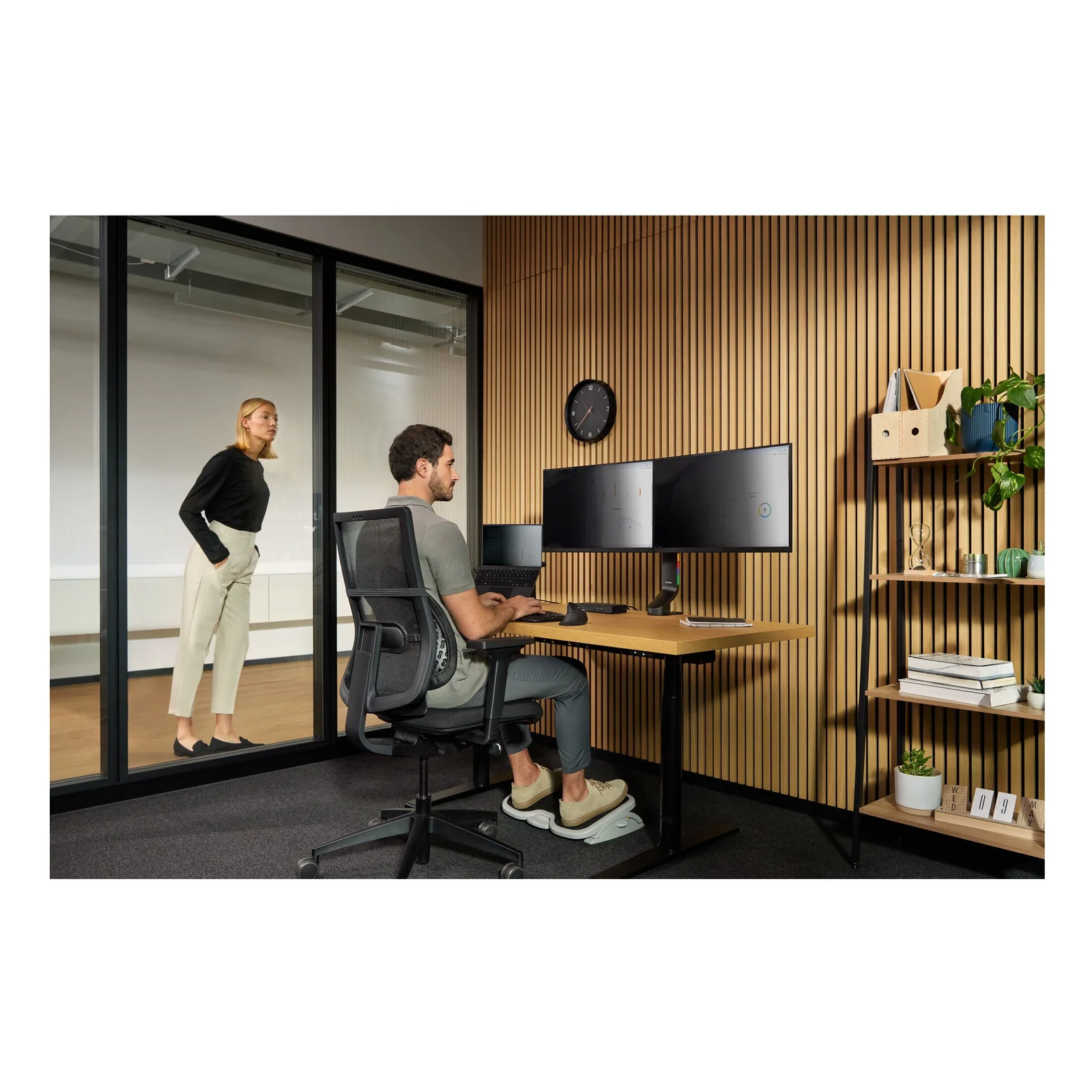 Utilisateur assis au bureau, double écran sur bras articulé, cloison vitrée, open space