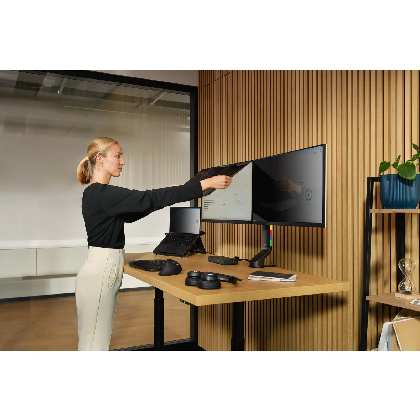 Femme ajustant la position d'un écran sur un bureau assis-debout à deux moniteurs