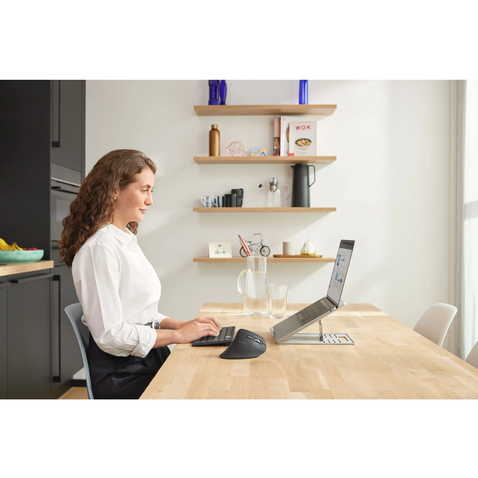Femme travaillant sur ordinateur portable à une table en bois clair, vue de côté