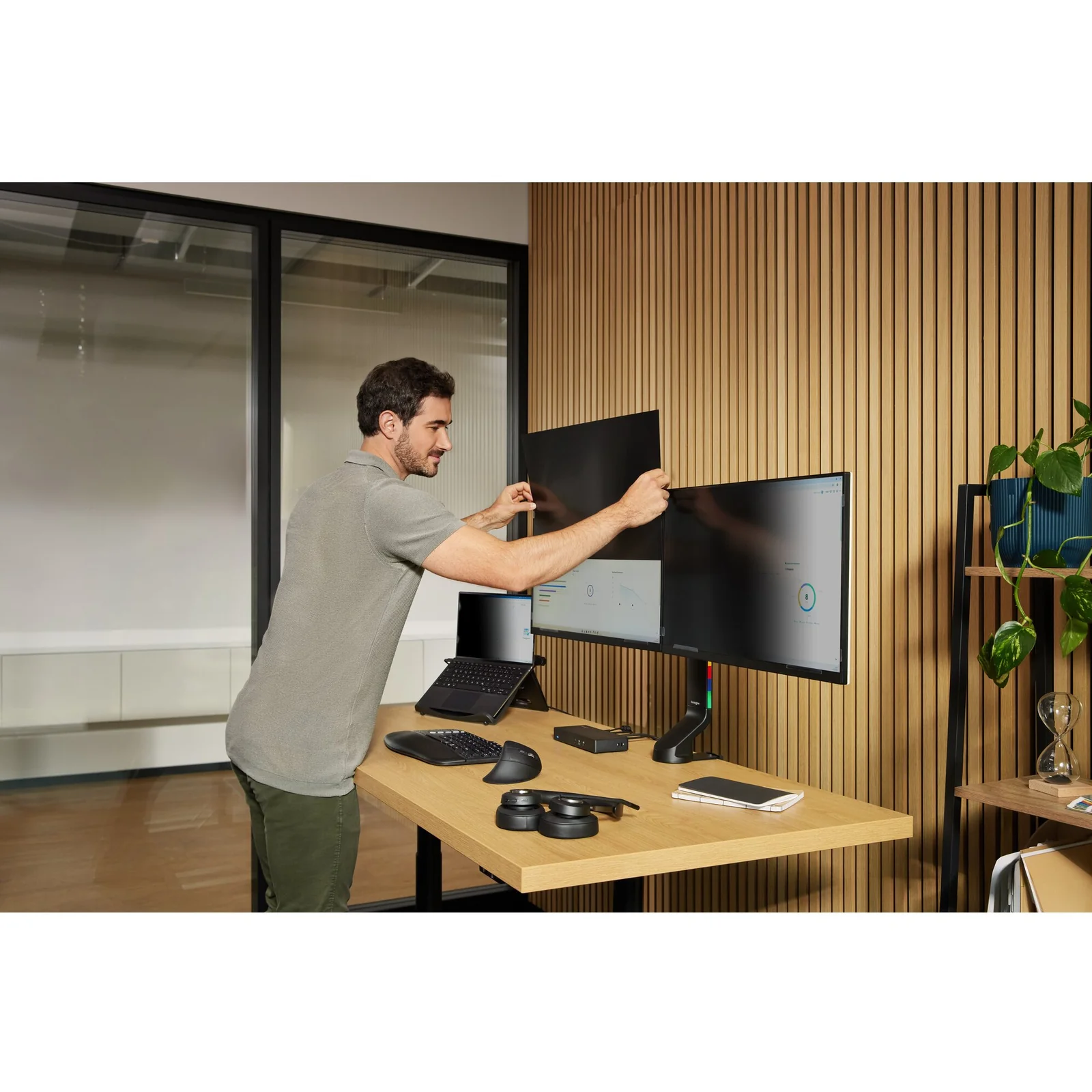 Homme debout réglant la position d'un écran sur un bureau assis-debout en open space