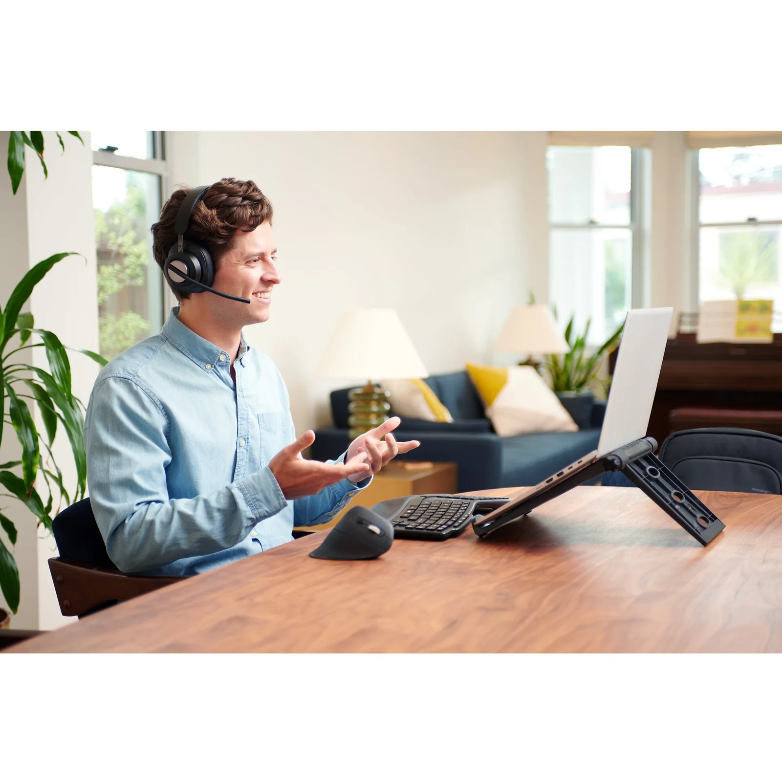 Homme avec casque audio travaillant sur ordinateur portable posé sur support, bureau en bois clair
