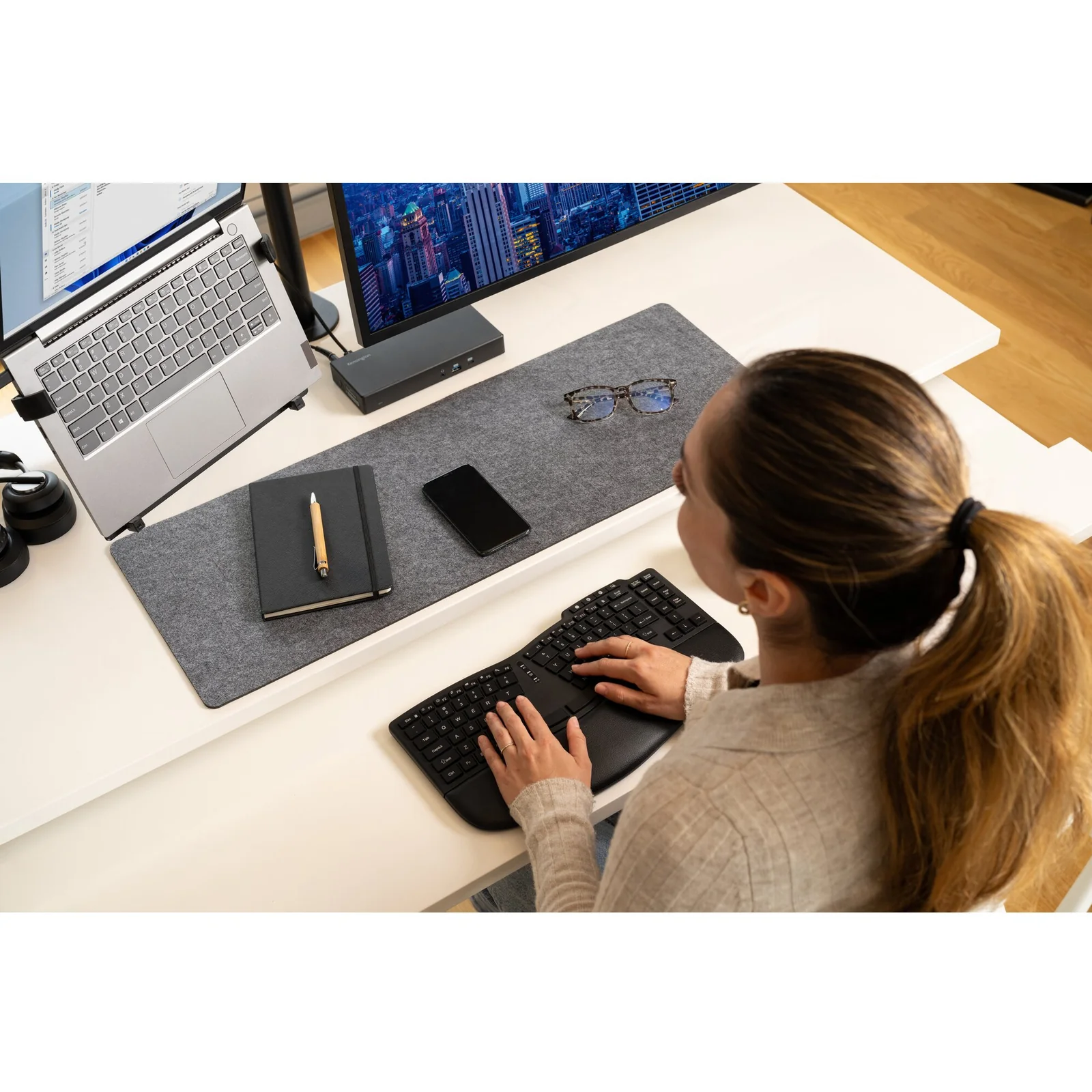 Femme de dos sur bureau avec station d'accueil Kensington, ordinateur portable et clavier sans fil