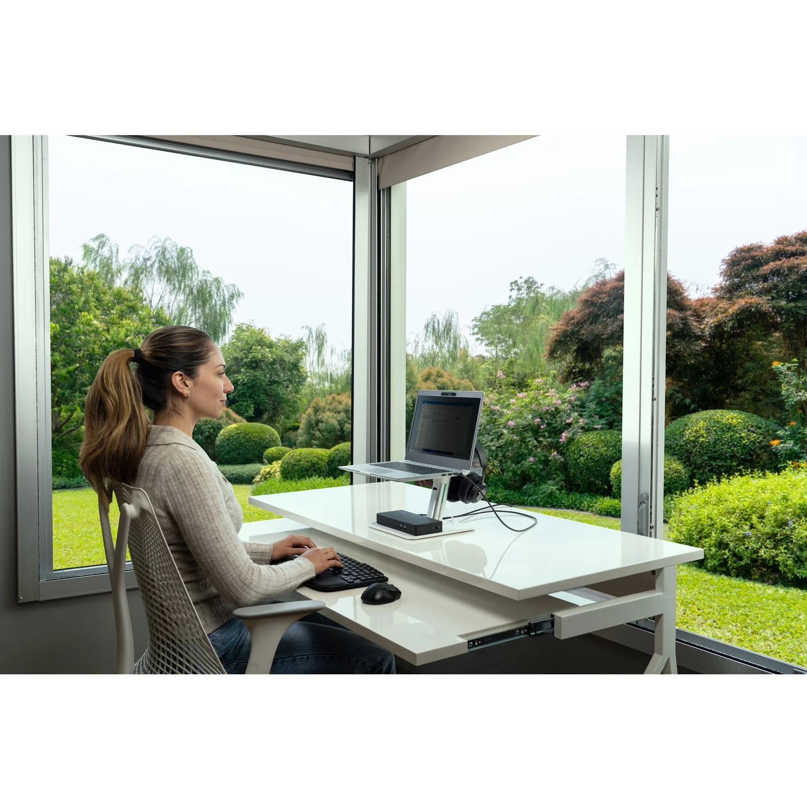 Femme utilisant station Kensington sur bureau en bois avec vue sur jardin, home office