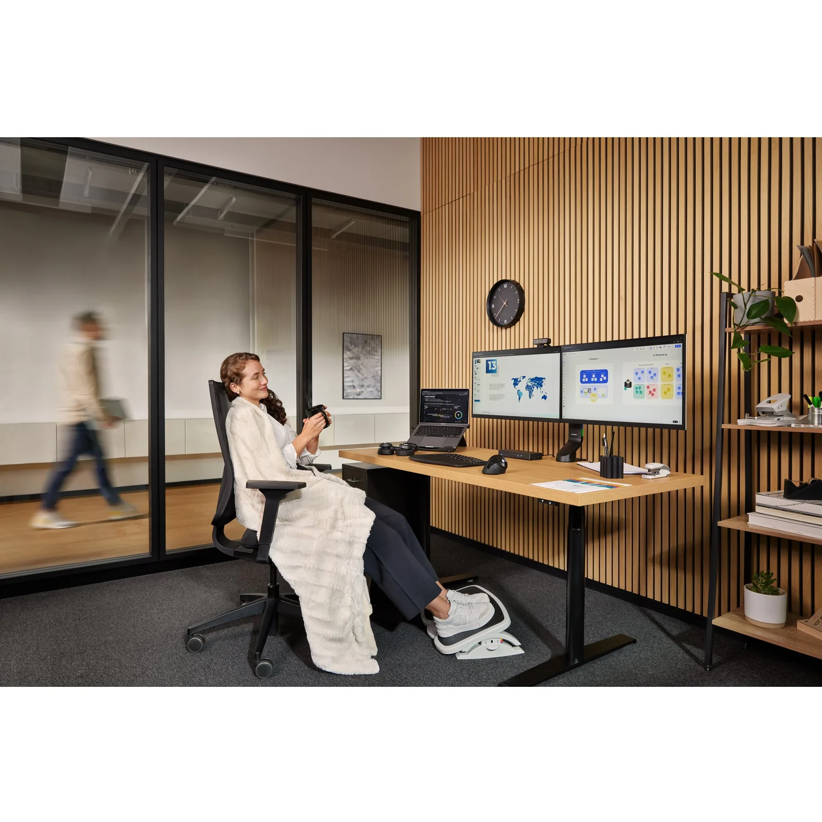 Femme assise à bureau ergonomique avec double moniteur et repose-pieds visible