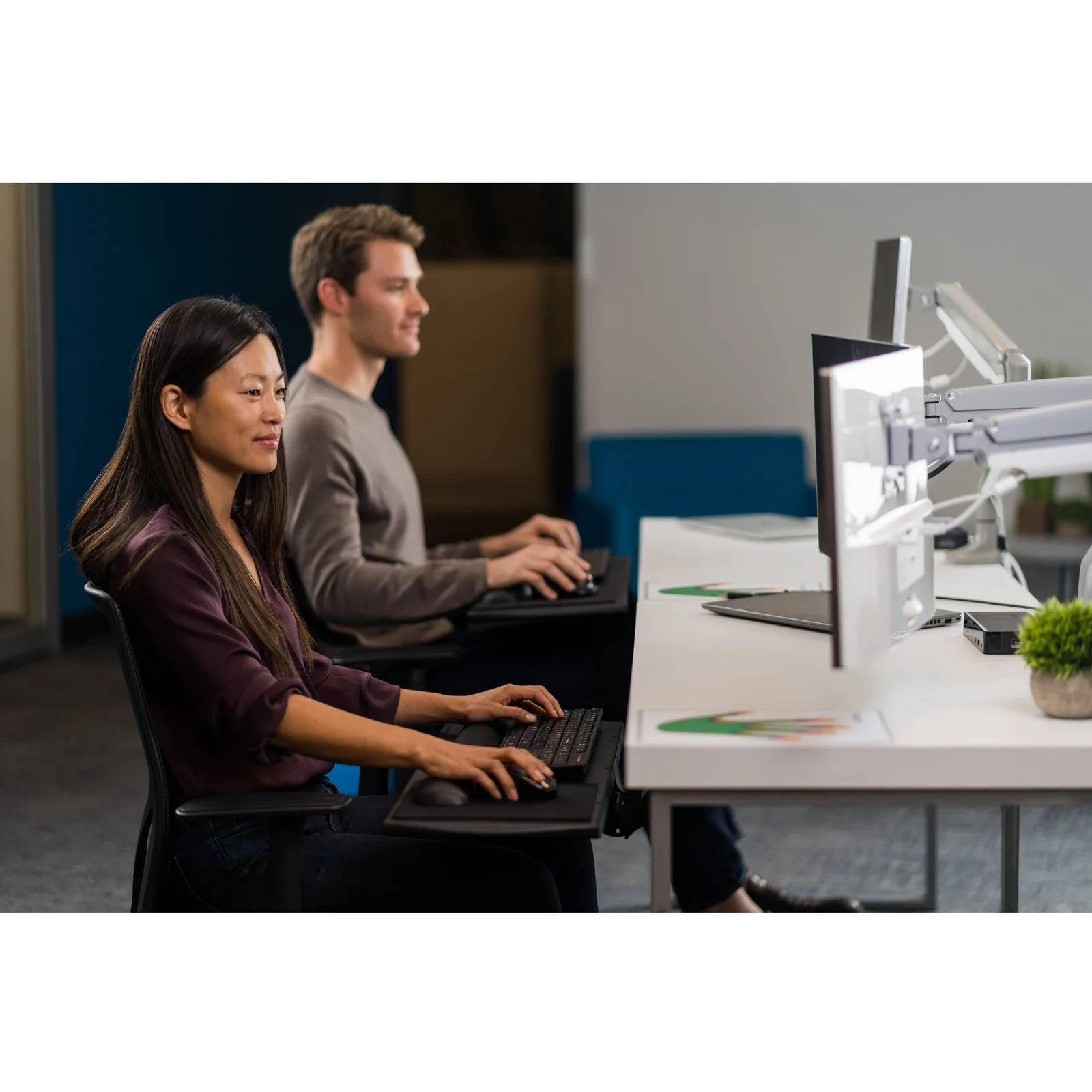 Deux collaborateurs côte à côte devant leur moniteur sur bras articulé, bureau open space
