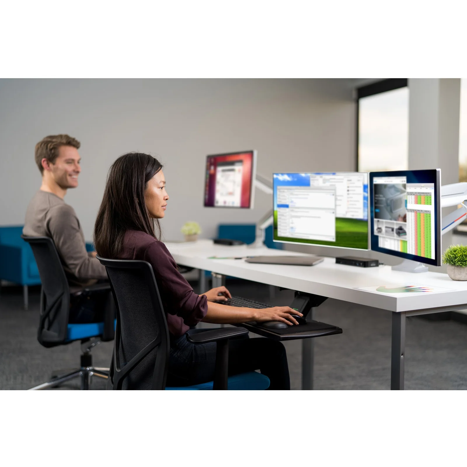 Utilisateur en bureau collaboratif, bras mono-écran, collègues visibles en arrière-plan