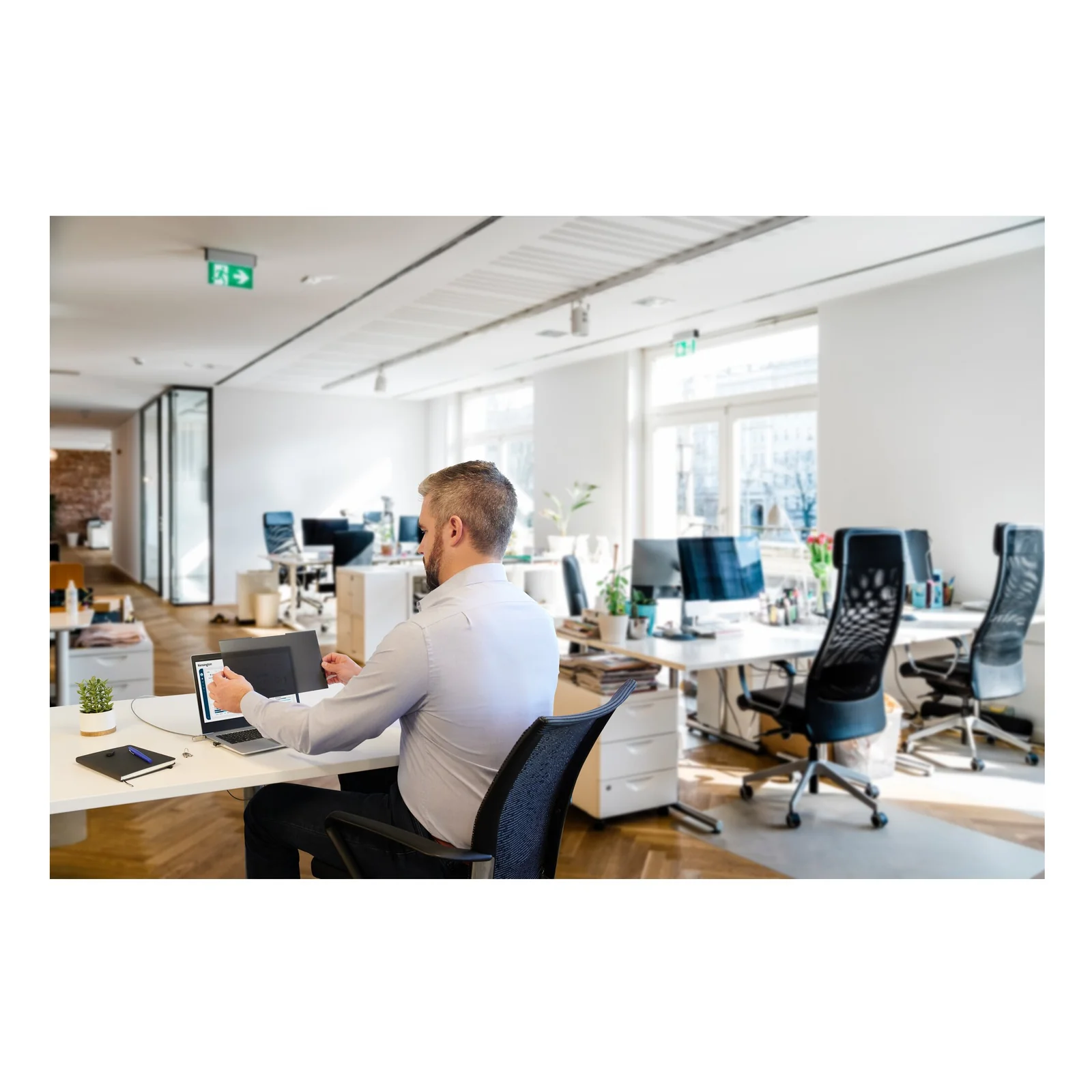 Homme assis dans un open space lumineux avec un laptop, environnement bureau
