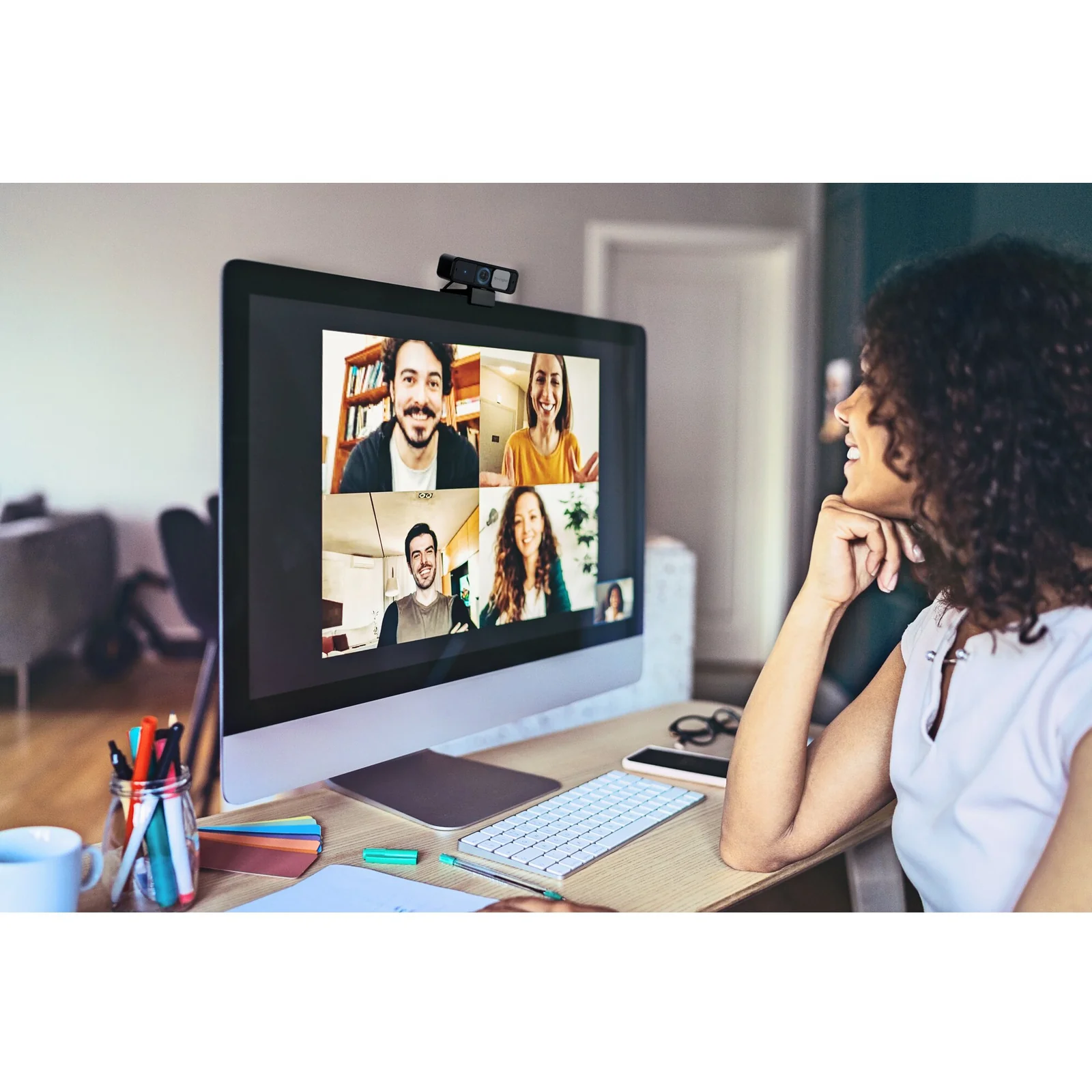 Femme en réunion vidéo multi-participants sur grand écran, webcam clipsée sur moniteur