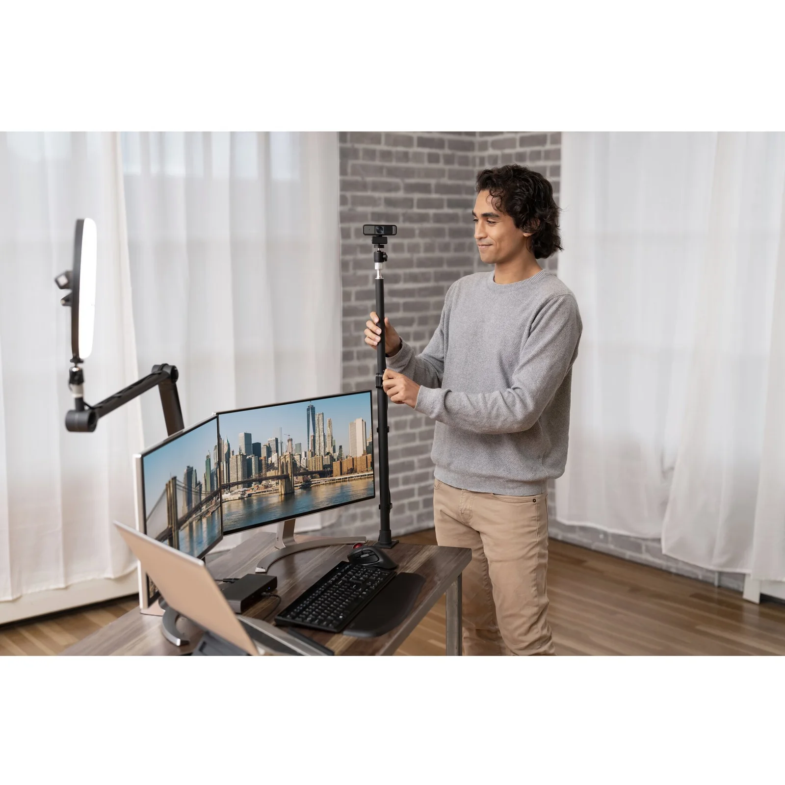 Homme ajustant une webcam sur bras articulé, double moniteur en arrière-plan